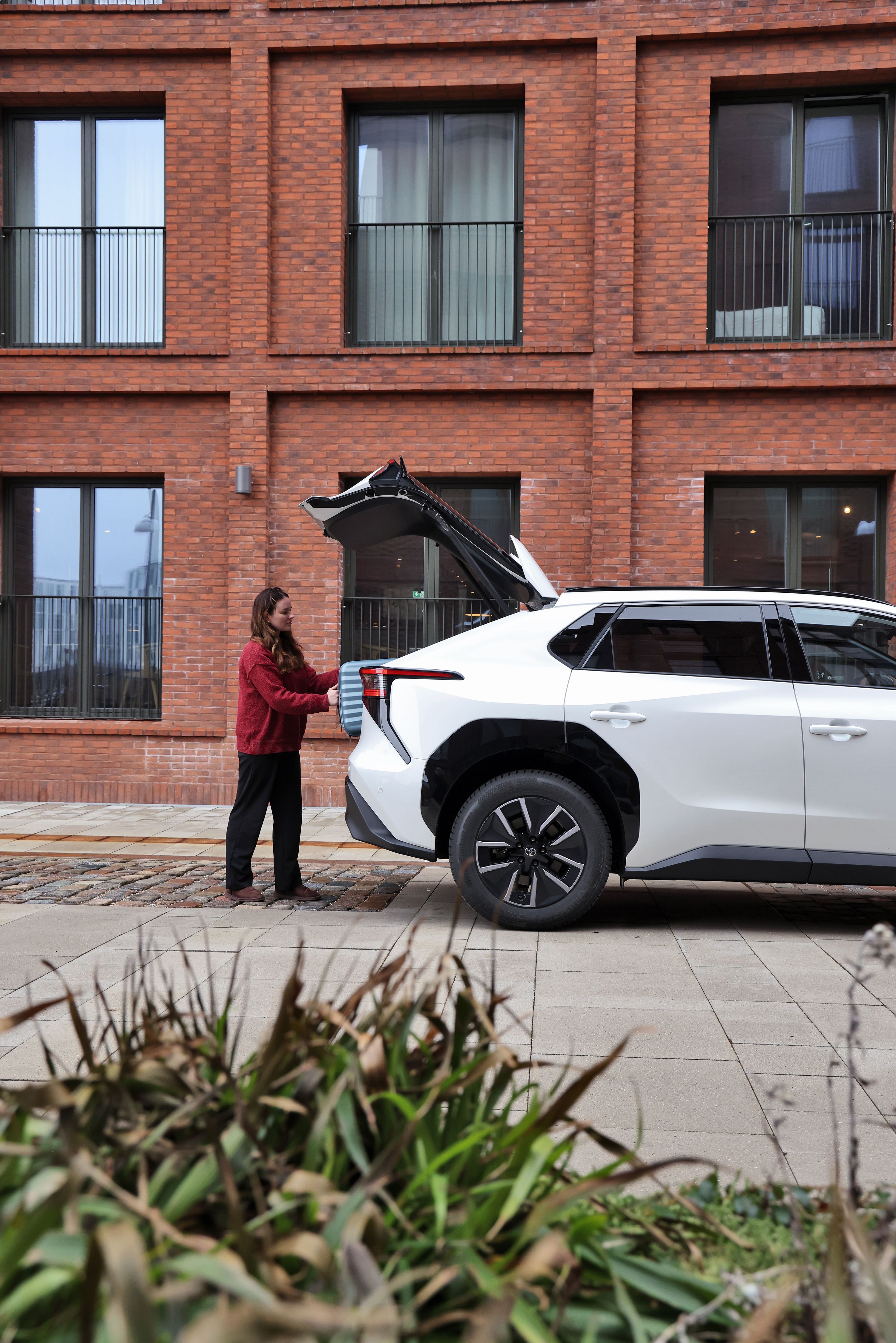 Kvinde lægger en kuffert i bagagerummet på en Toyota bZ4X