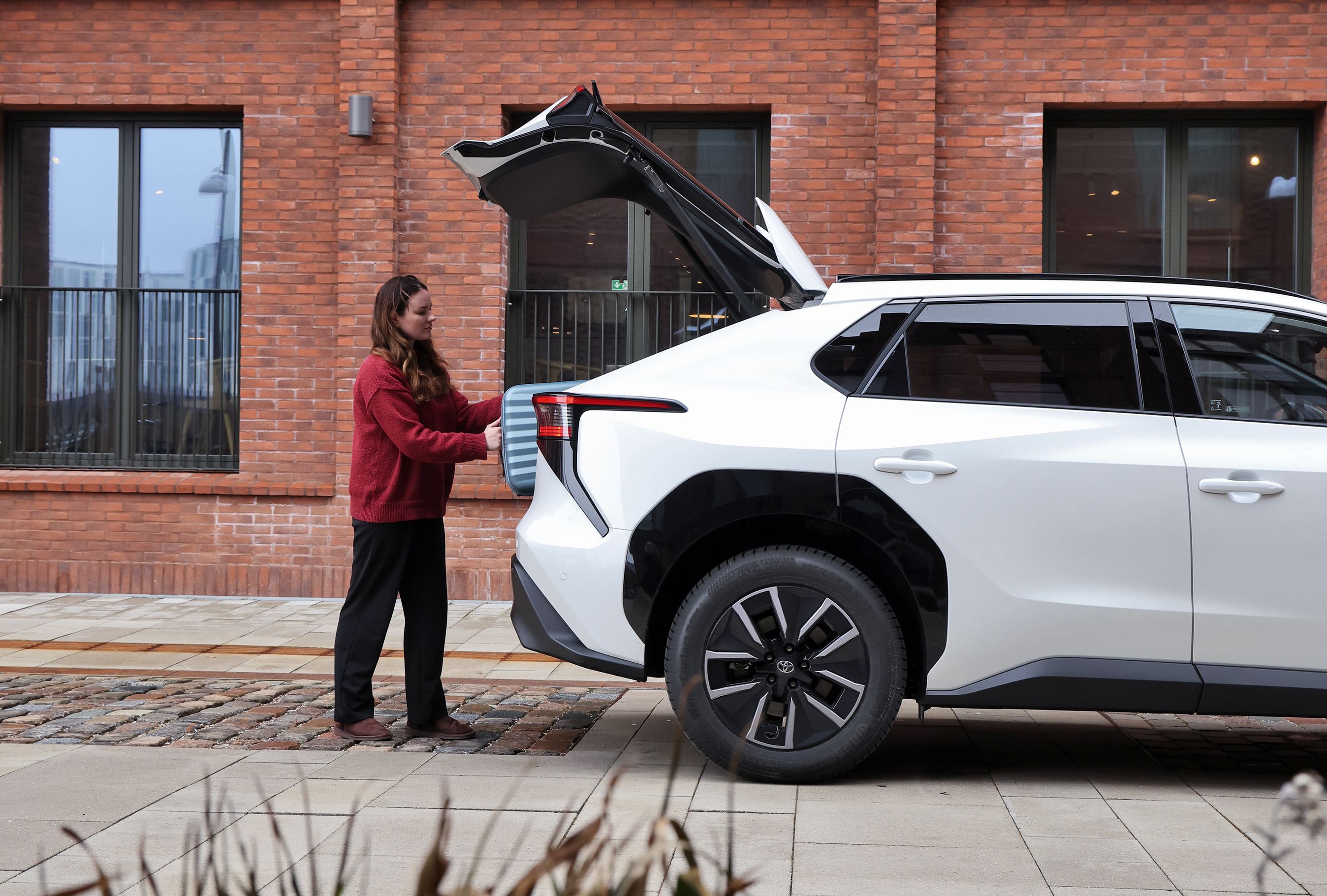 Kvinde lægger en kuffert i bagagerummet på en Toyota bZ4X