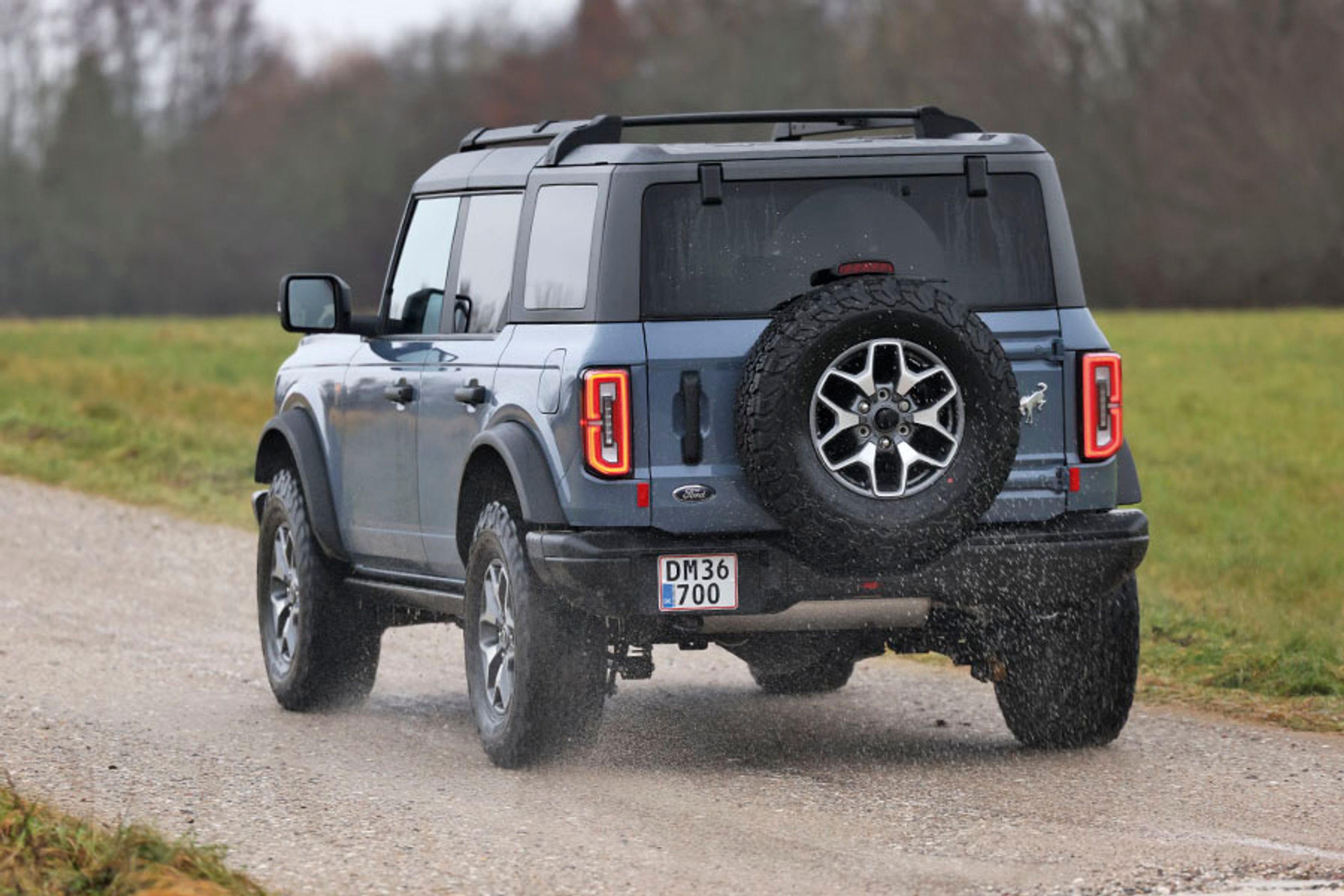 En Ford Bronco set bagfra, mens den kører på en landevej med græs i baggrunden.