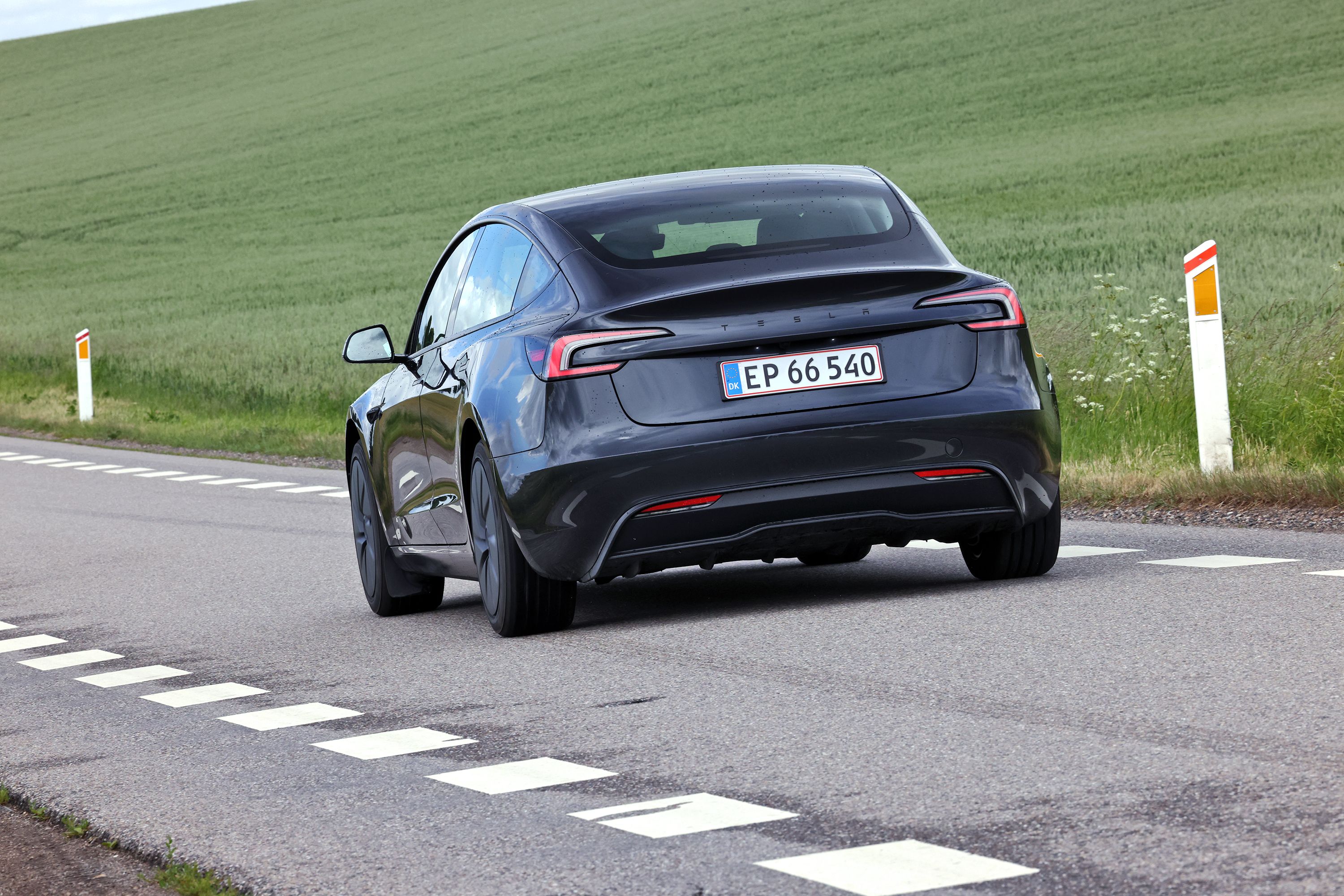Tesla Model 3 baghjulstræk 2026 set bagfra på landevej med grønne marker i baggrunden. 