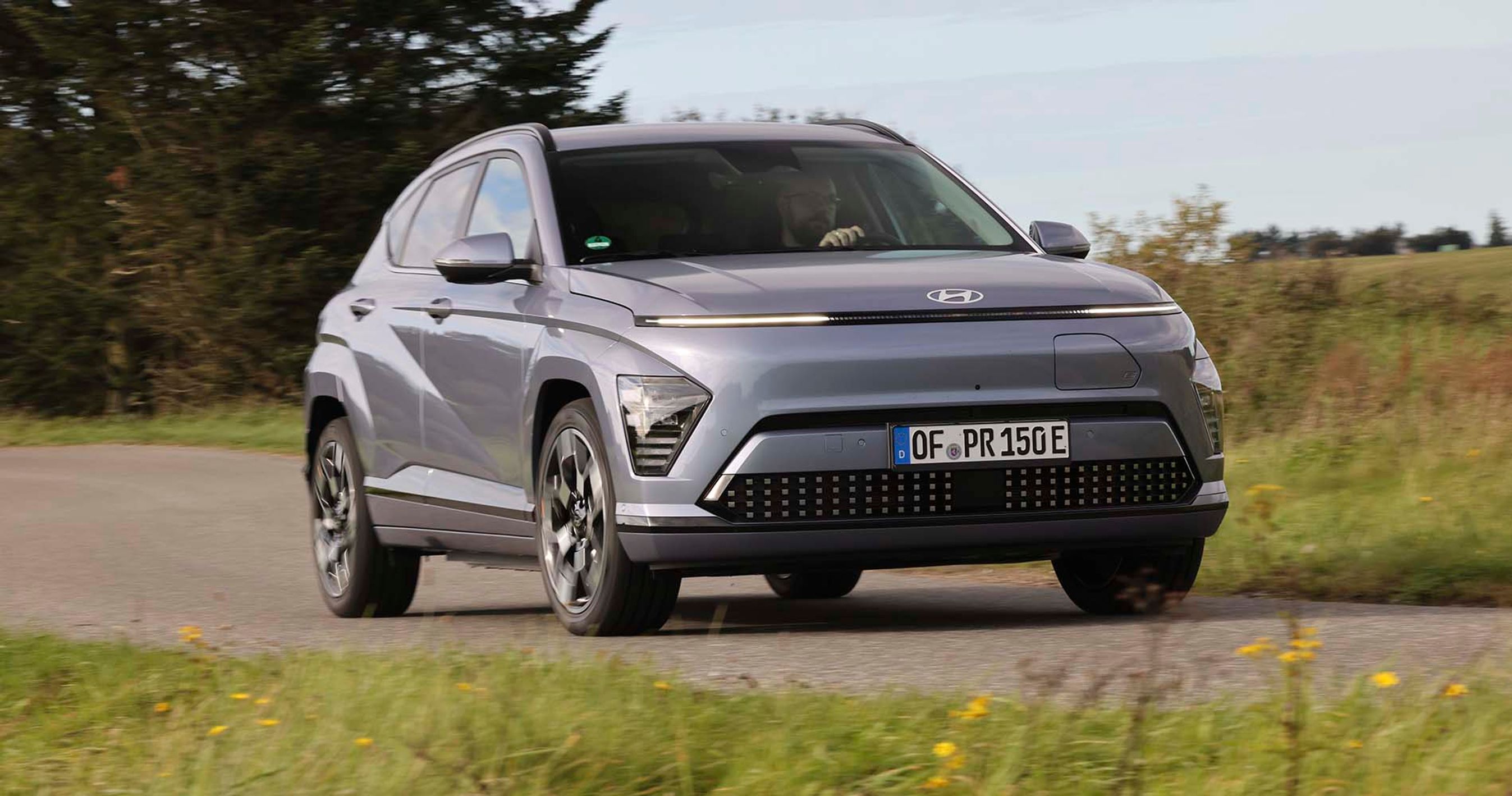 Elbilen Hyundai Kona kører på en landevej med græs foran og bagved.