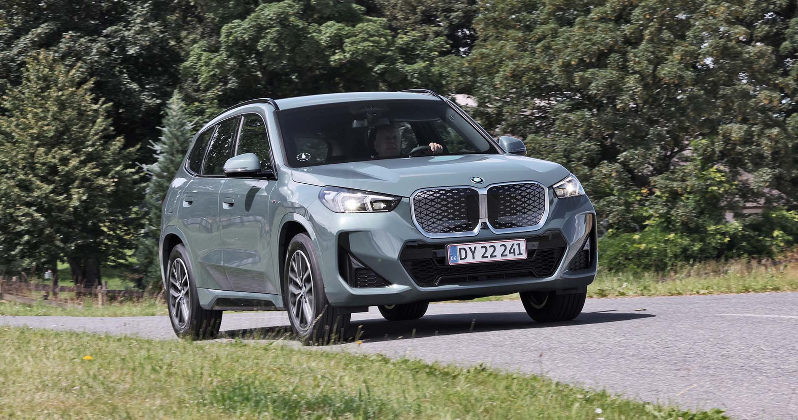 BMW iX1 kører på en vej med træer i baggrunden