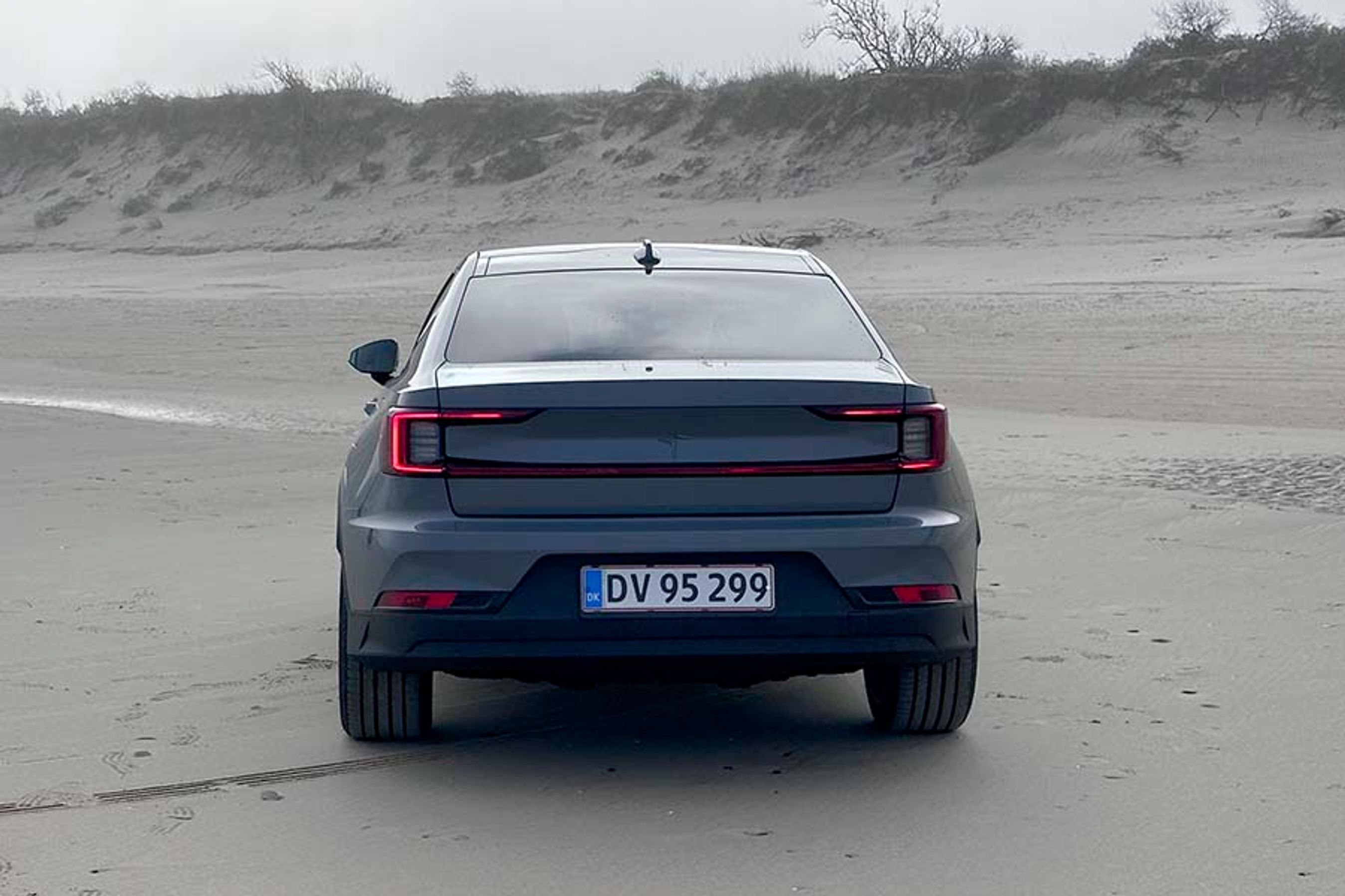 Polestar 2 set bagfra, mens den holder foran klitterne på en strand