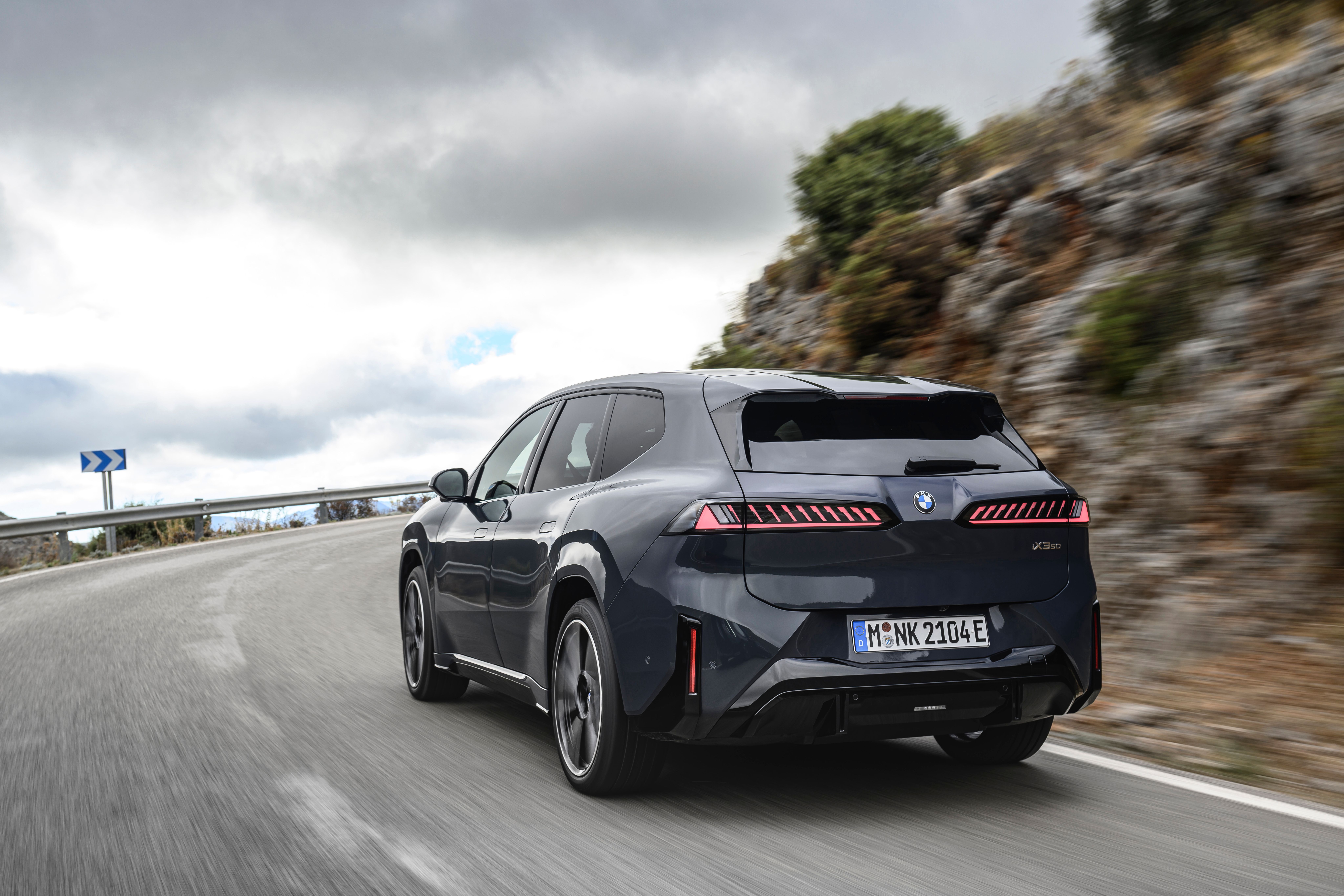 BMW iX3 set bagfra, mens den kører i et sving på en bjergvej
