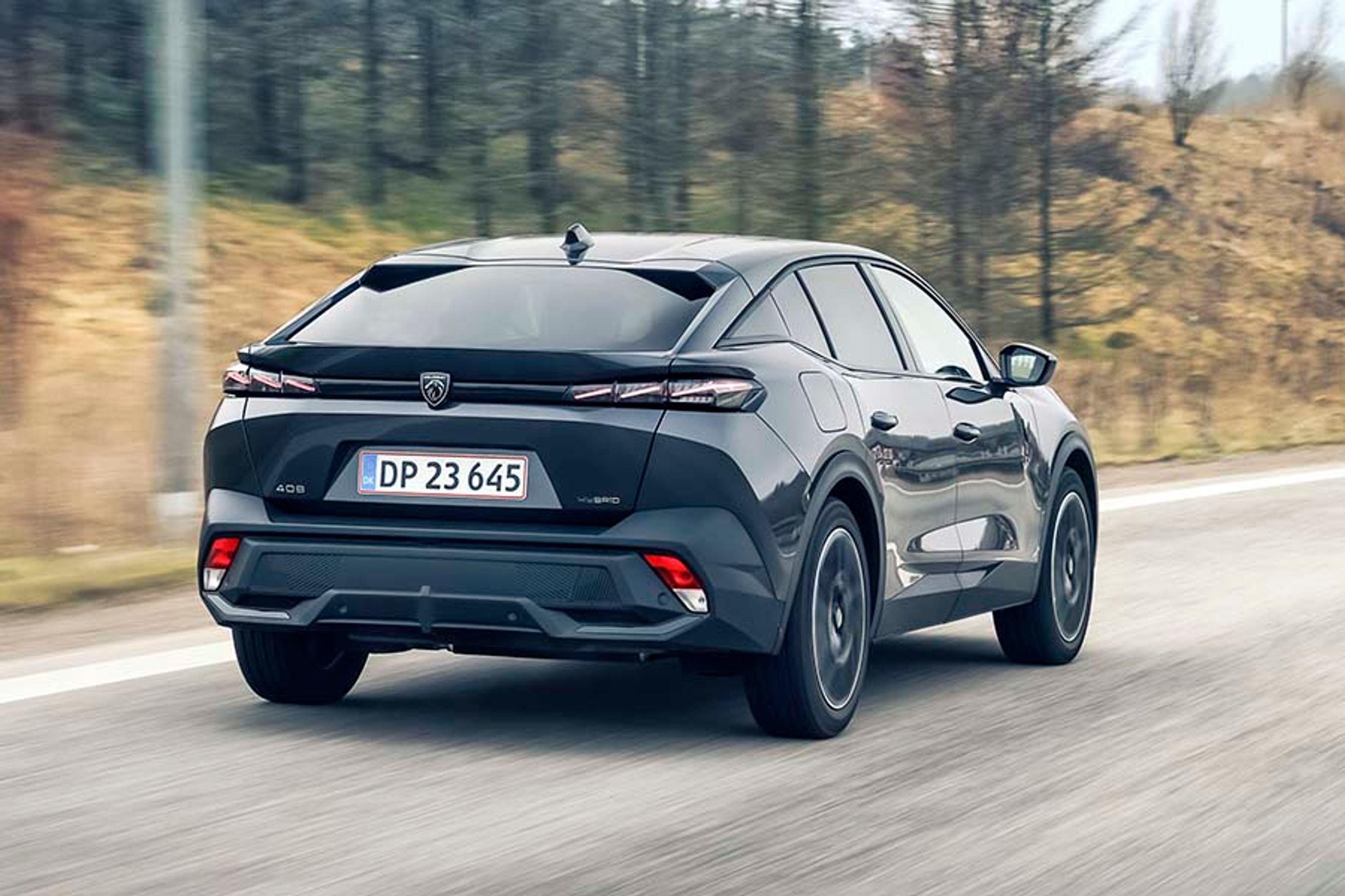 Peugeot 408 set bagfra, mens den kører på en landevej med træer i baggrunden