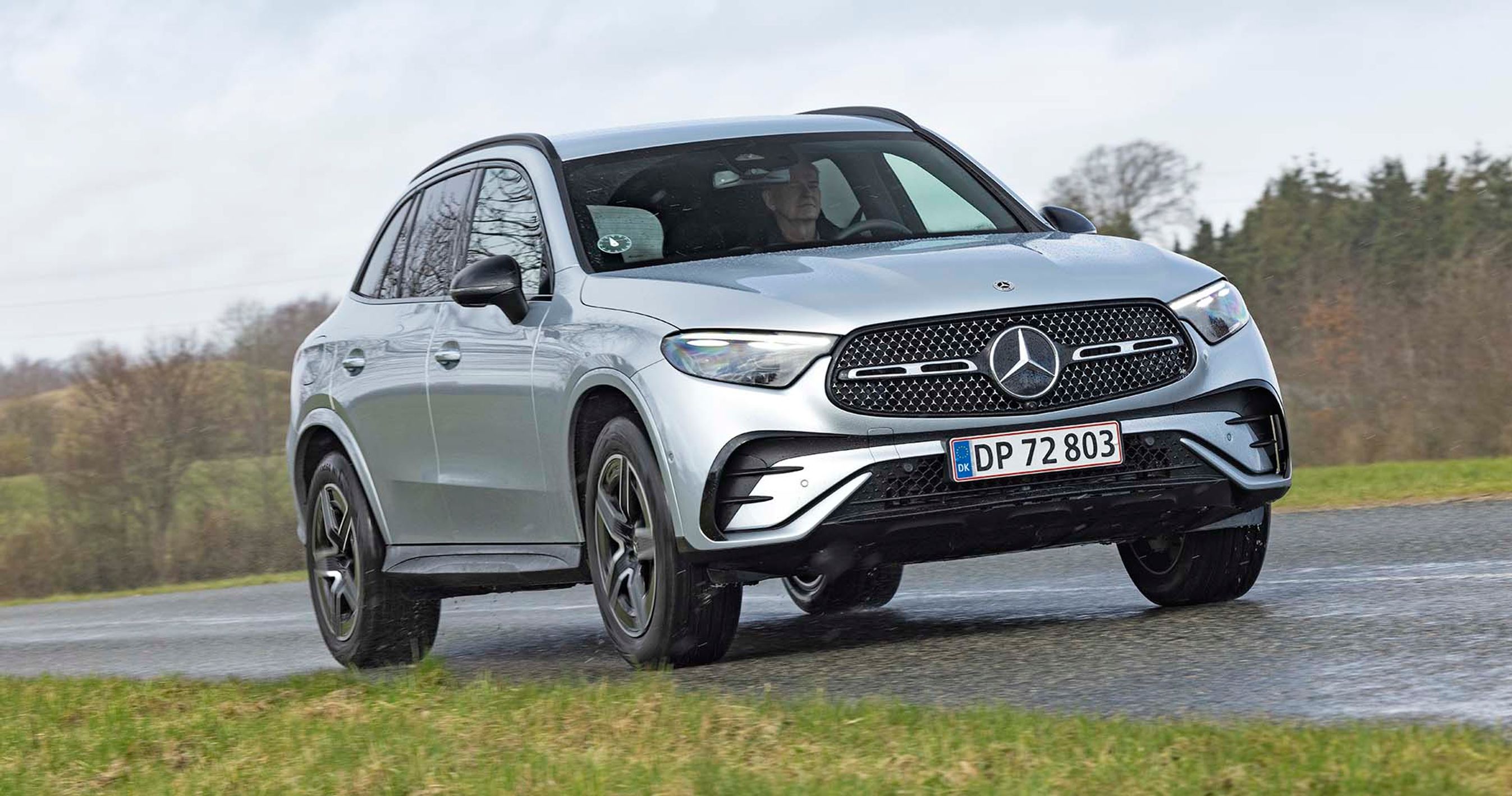 En sølvgrå Mercedes GLC kører på en landevej med skov i baggrunden