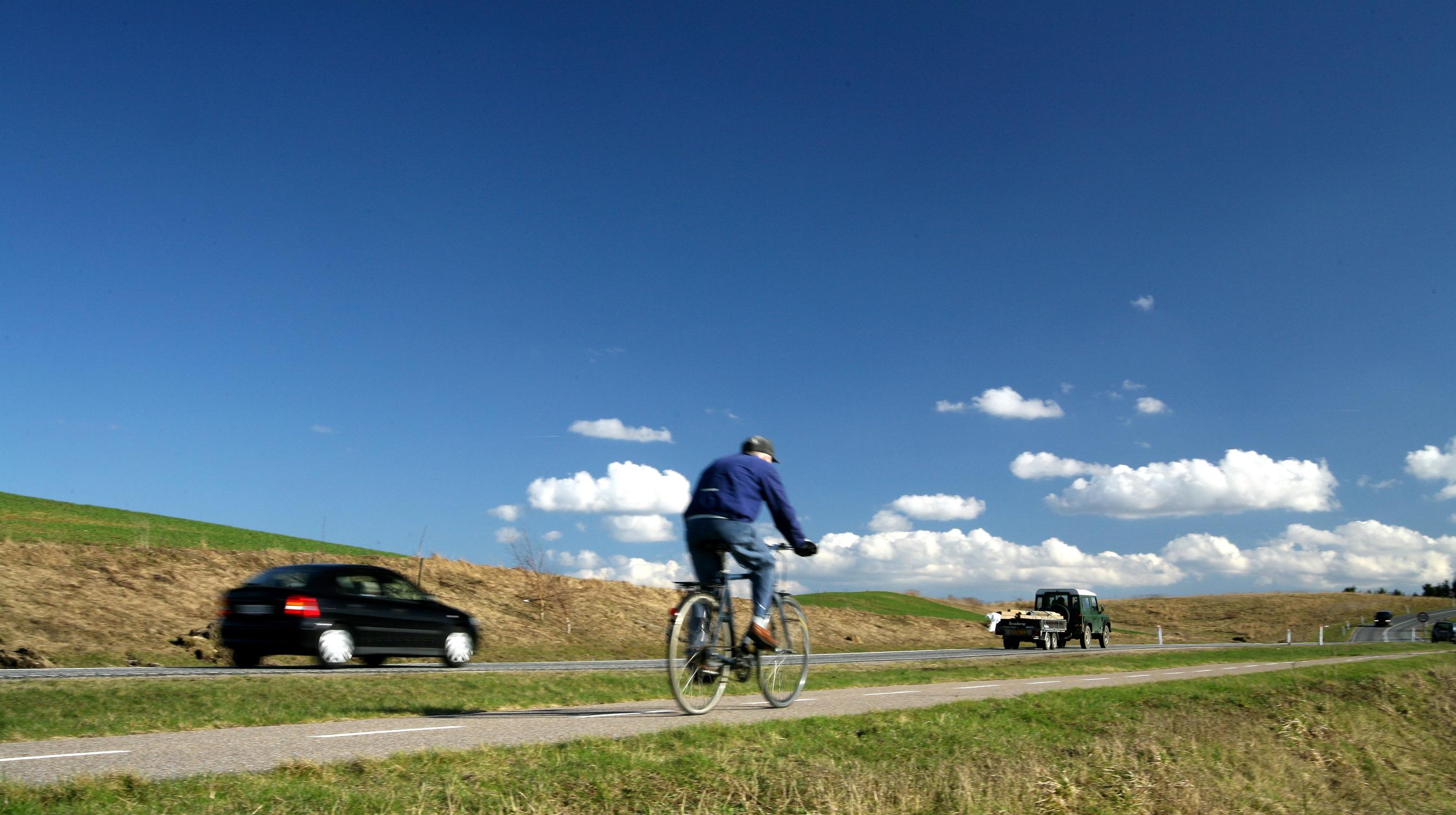 Cykel på cykelsti og tre biler kører på en landevej.