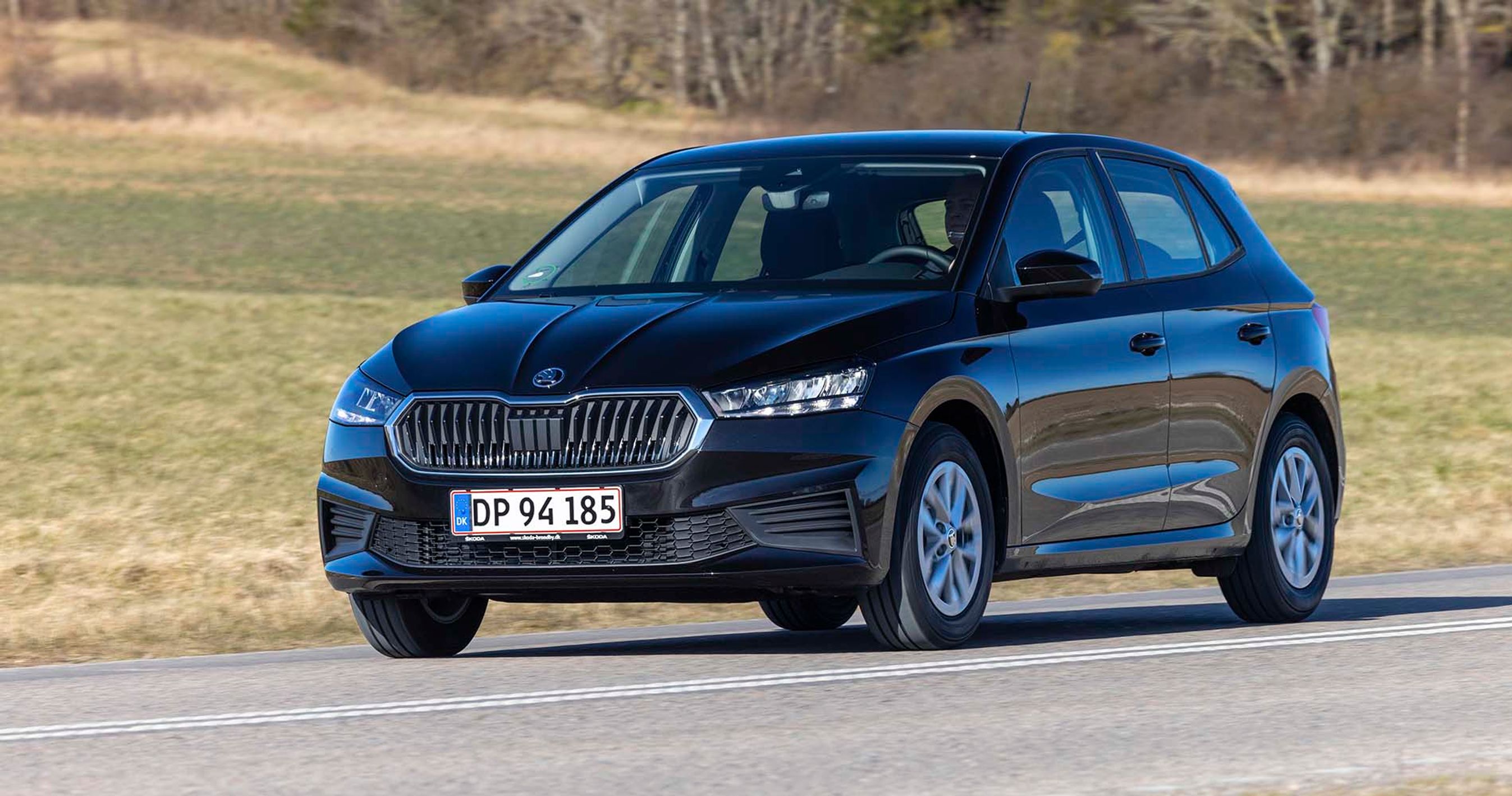 En sort Skoda Fabia kører på en landevej med græs i baggrunden