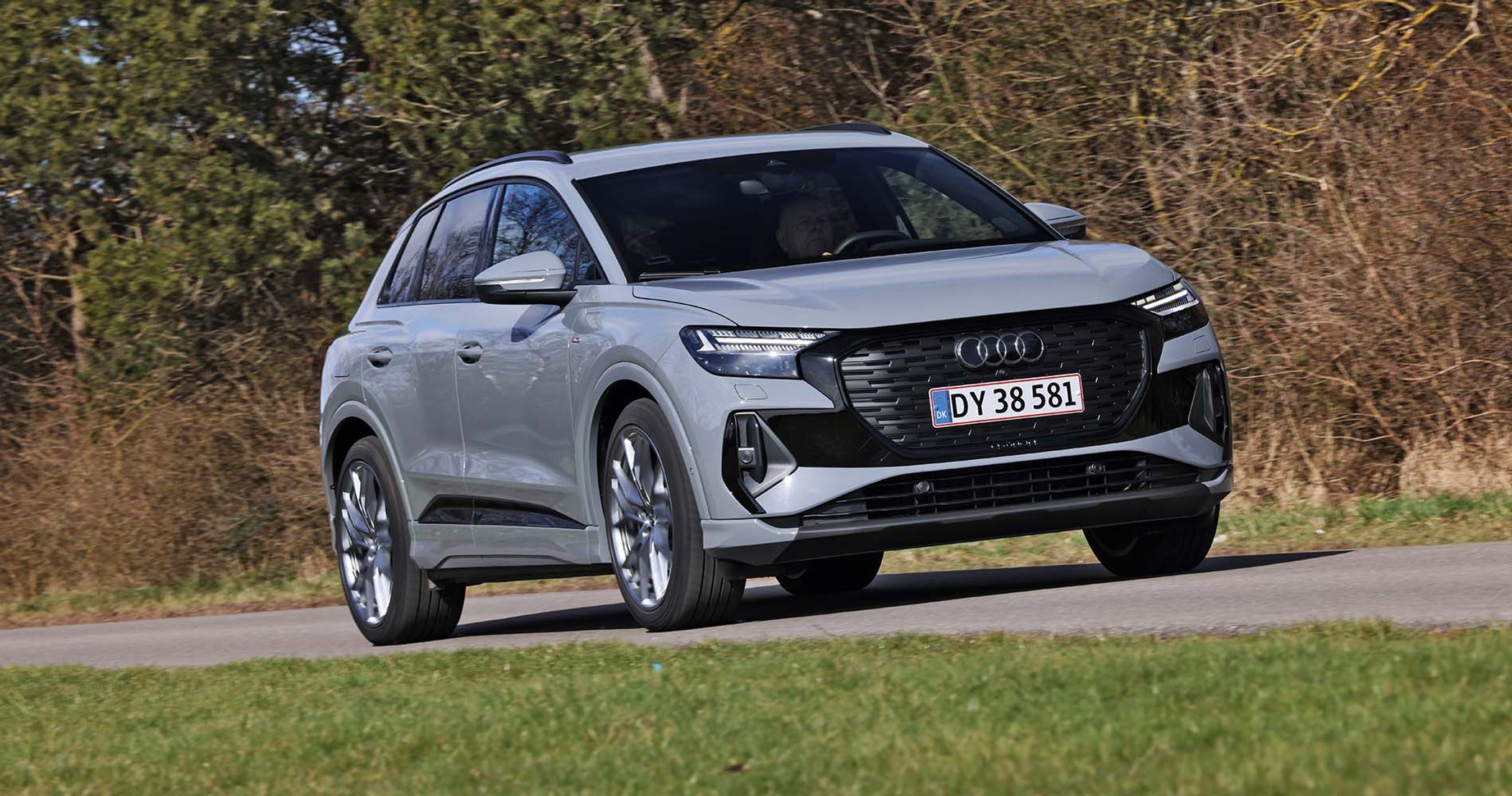 En Audi Q4 e-tron kører på en landevej med græs i forgrunden