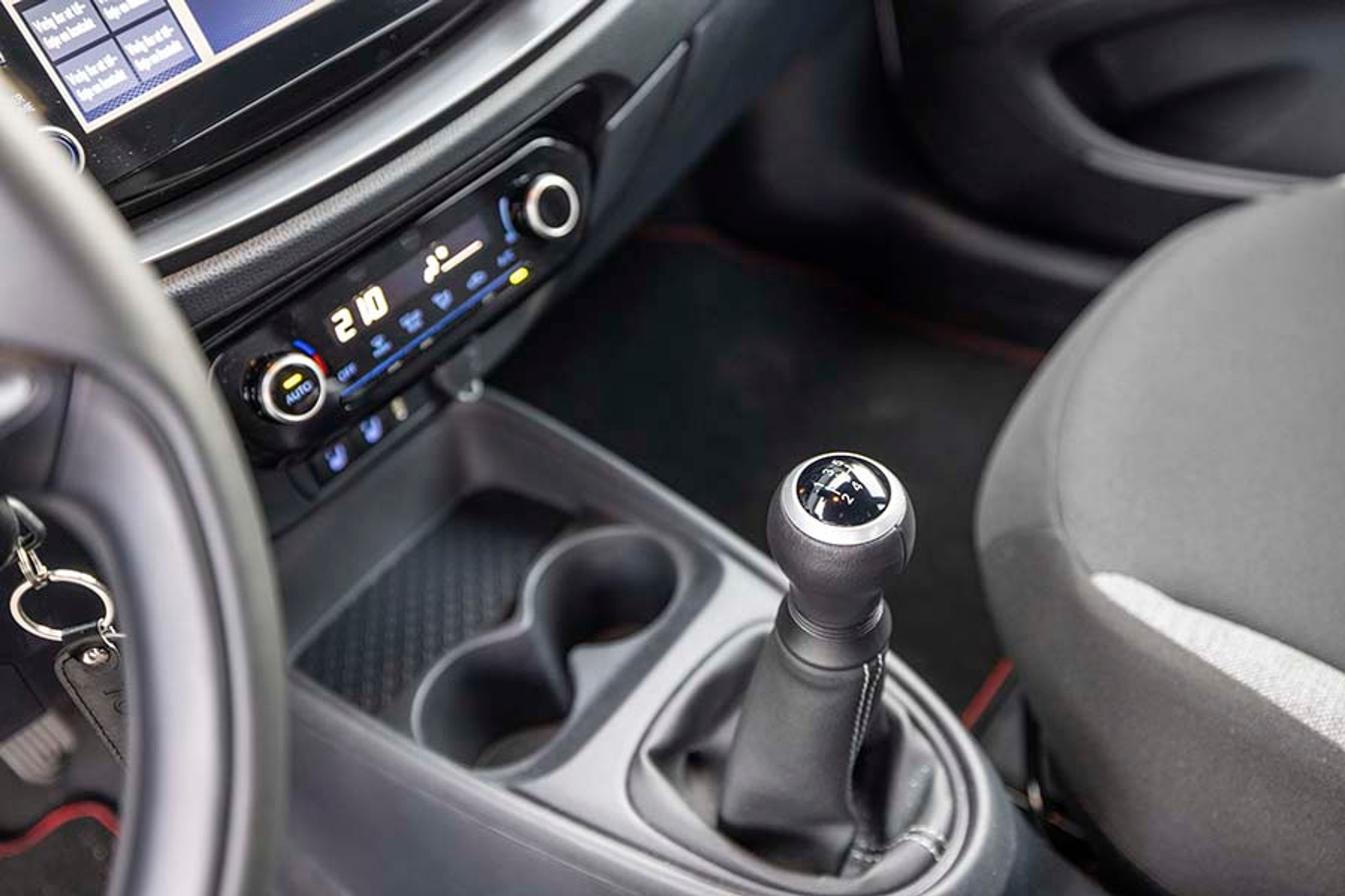 Der er fem gear i bilen, og der er gode fralægningsmuligheder foran gearstangen. Bemærk det digitalt indstillelige klimaanlæg.