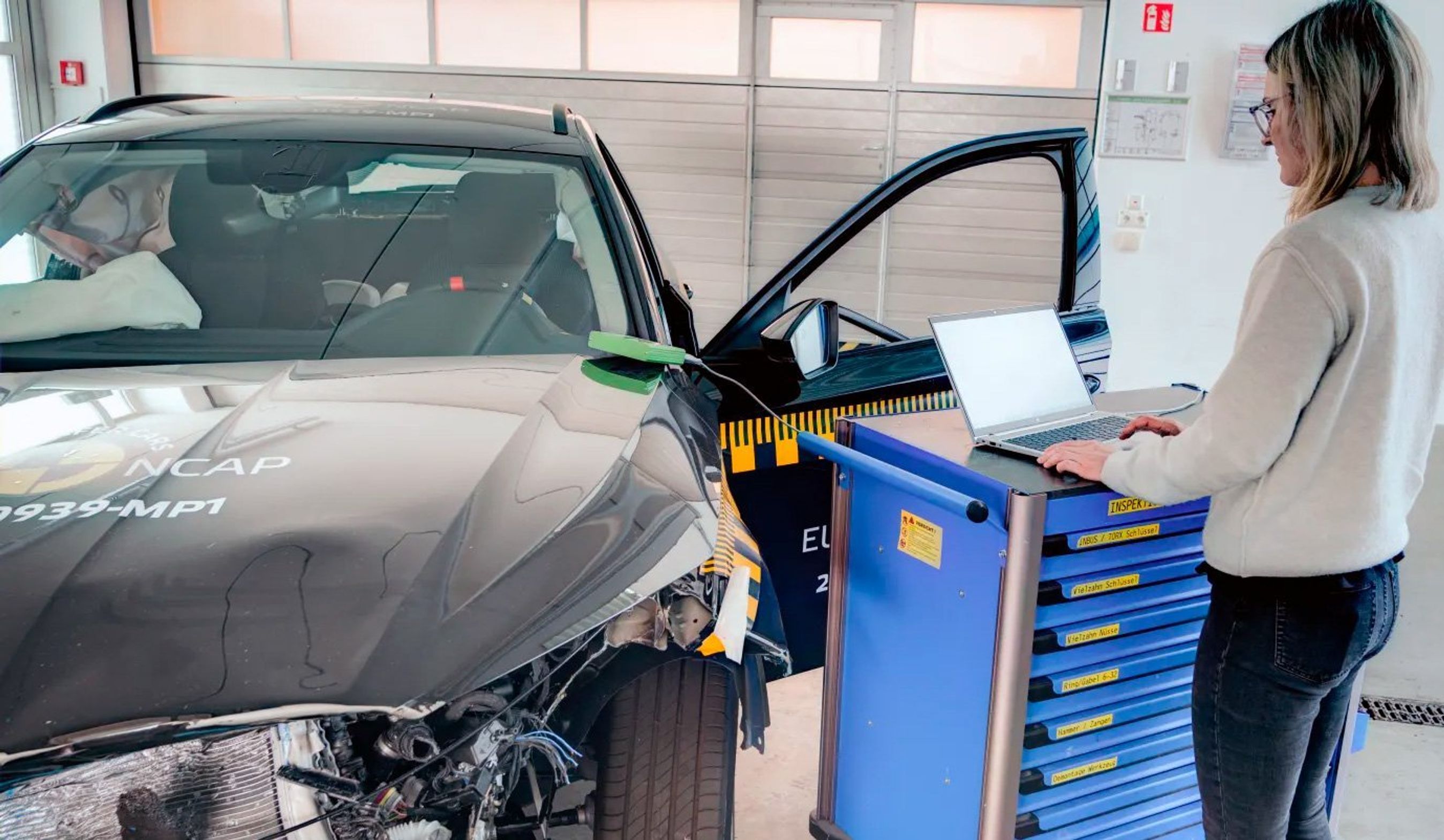 Smadret bil med tilkoblet pc og person i forgrund.