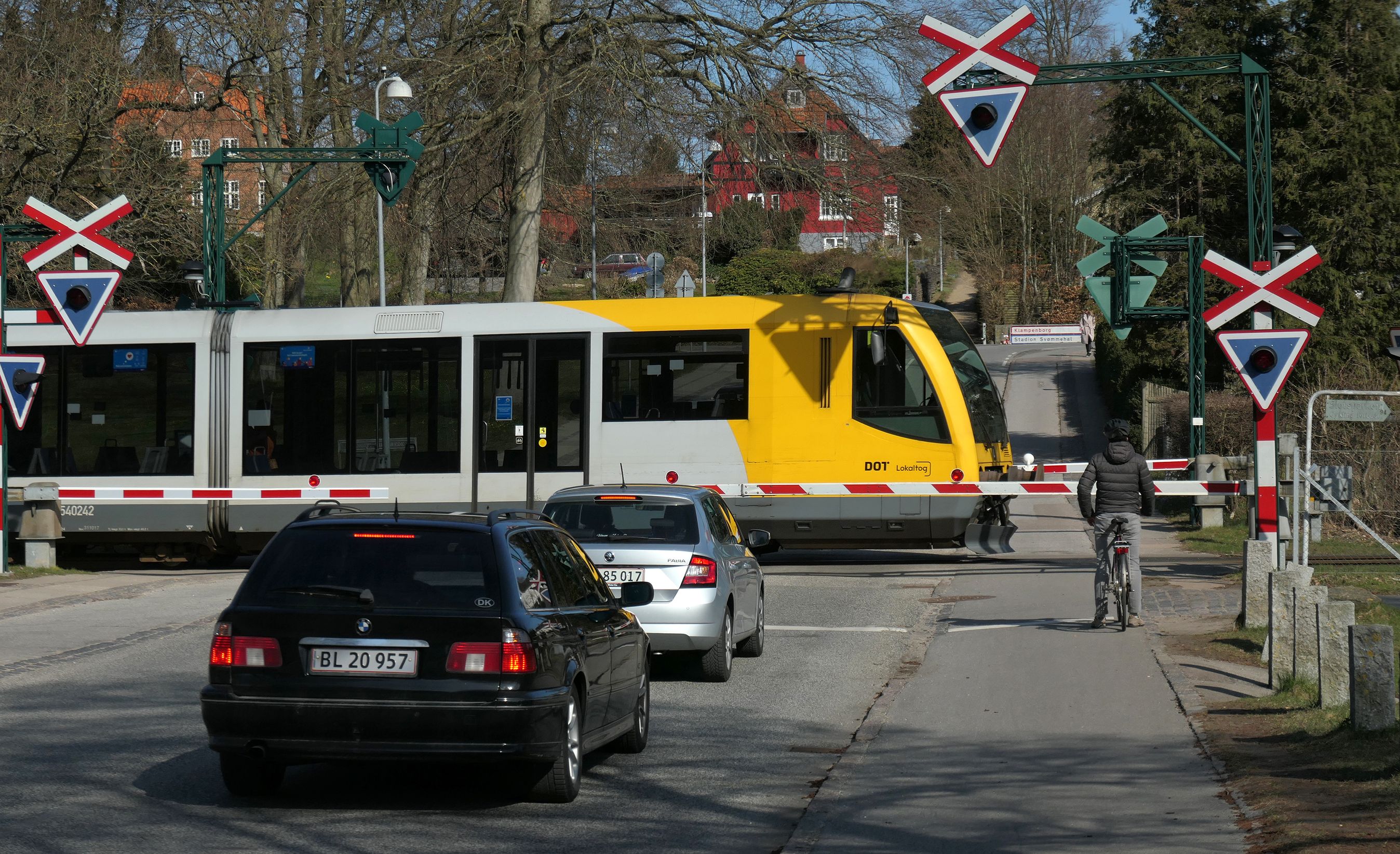 Biler der holde i kø ved jernbaneoverkørsel med krydsende tog.