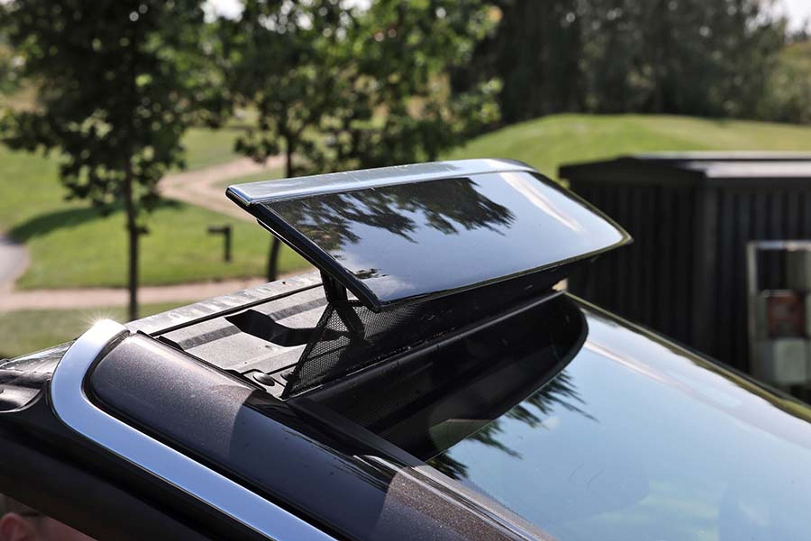 Den lille skærm med et net hen over forruden både løfter vinden over forreste række og sørger for, at der ikke er for meget turbulens bagtil. Den kører op ved et tryk på en knap, og ved samme lejlighed kommer et lille vindnet op lige bag hovedstøtterne ved bagsædet.