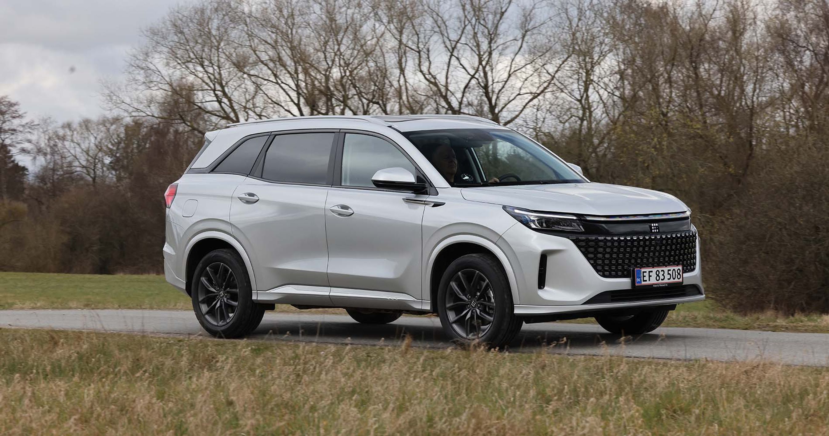 Navor E5 set fra siden, mens den kører på vej med træer i baggrunden.