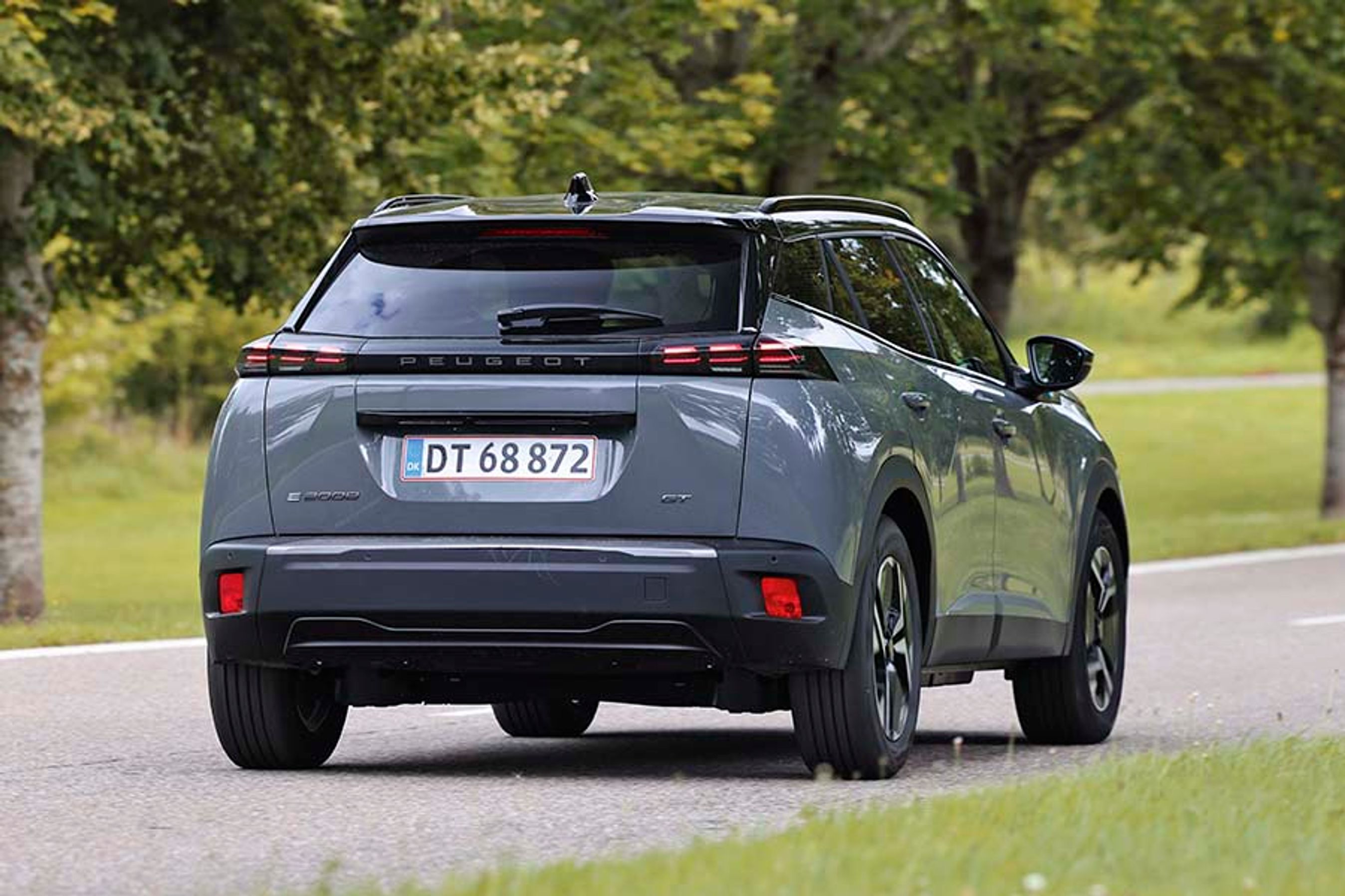 Elbilen Peugeot E-2008 set bagfra, mens den kører ned ad en landevej med træer i baggrunden.