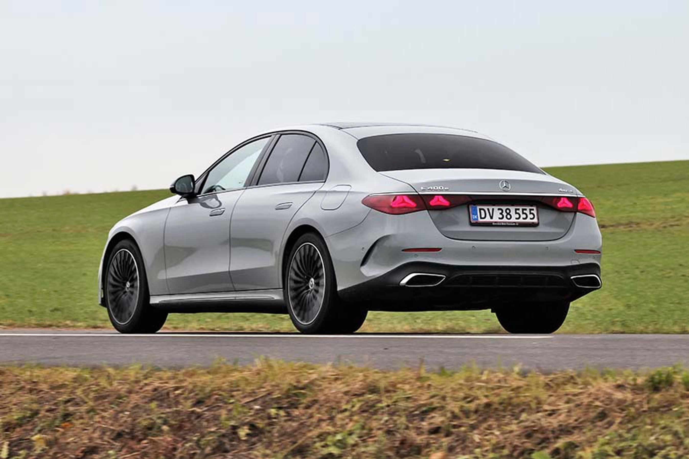 En sølvgrå Mercedes E-klasse set bagfra, mens den kører på en vej med græs i baggrunden