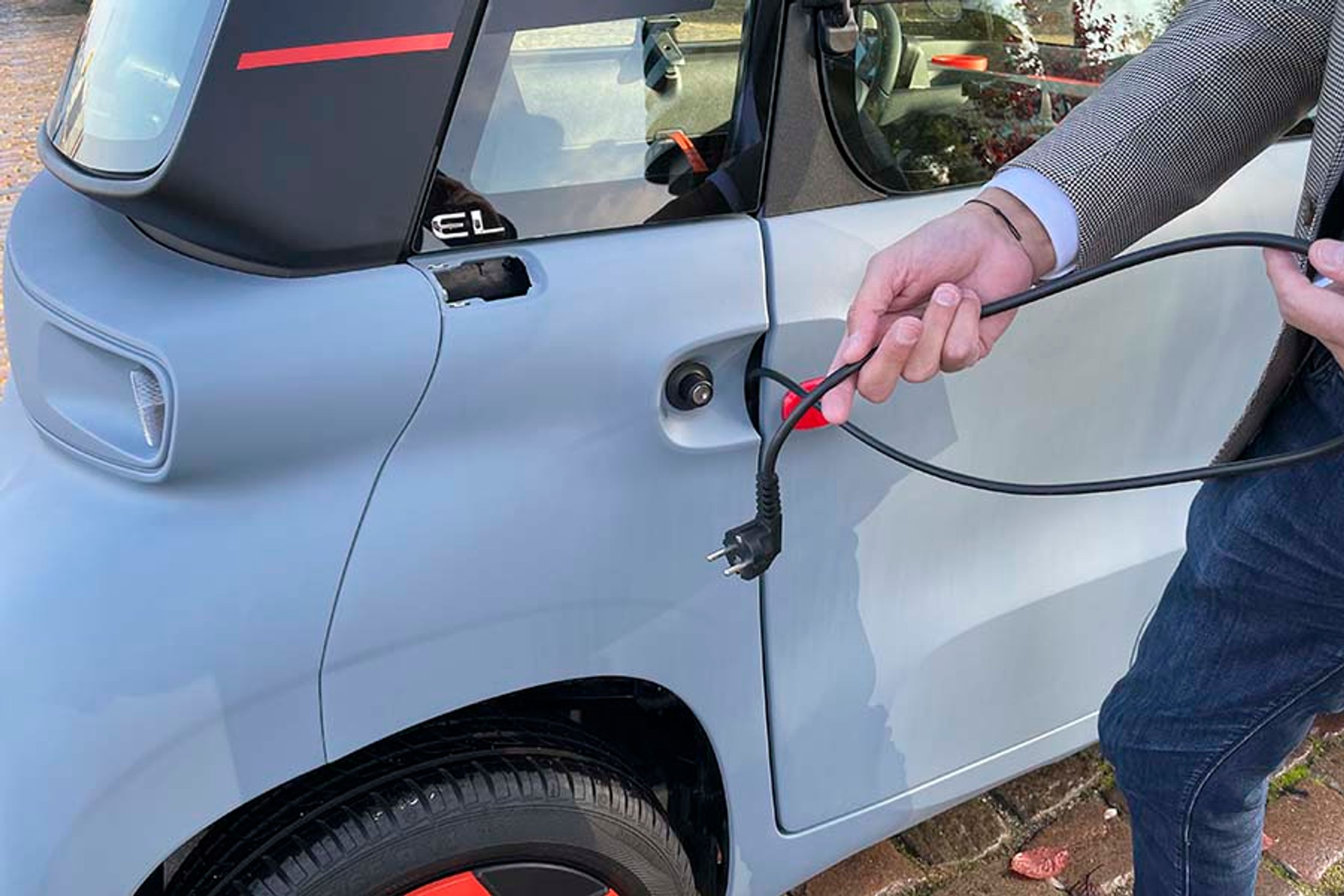 Ladeledningen er indbygget i dørstolpen, men ledningen kan ikke selv rulle ind efter brug. Den skal proppes ind.