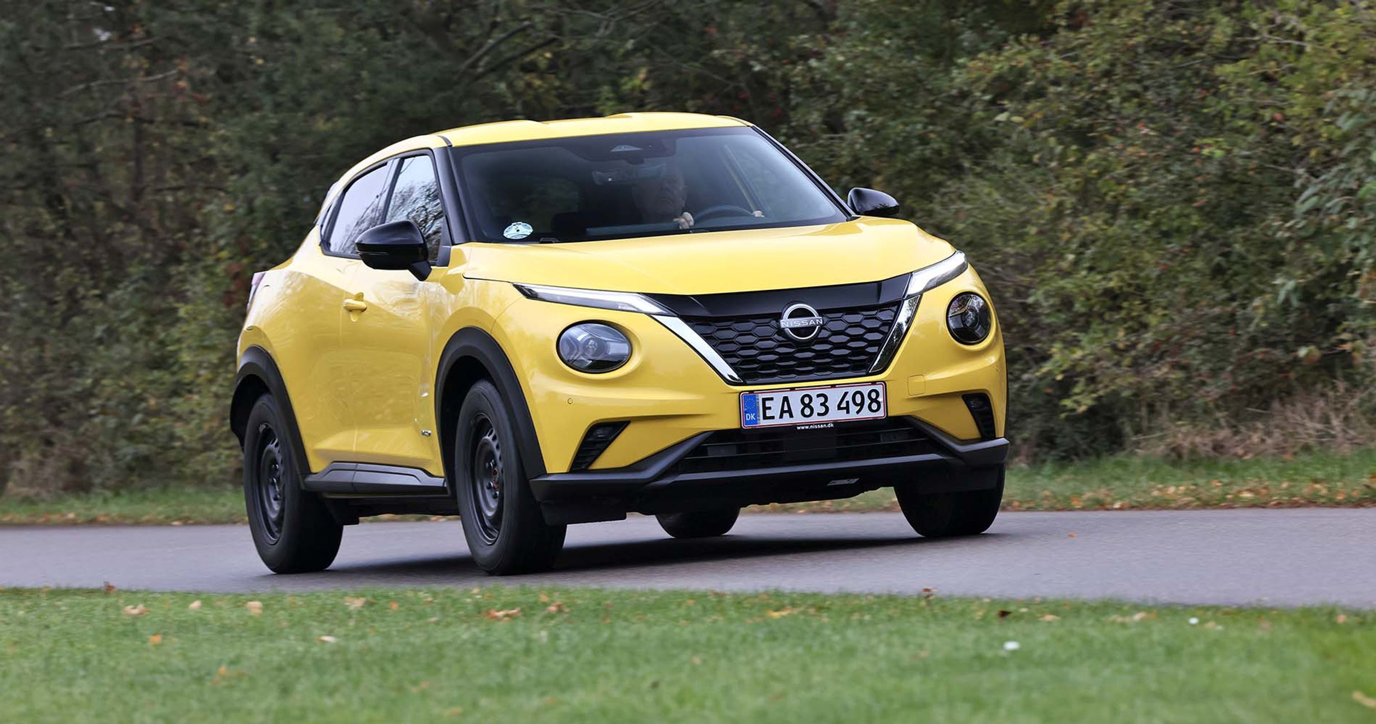 Gul Nissan Juke kører på landevej med træer i baggrunden