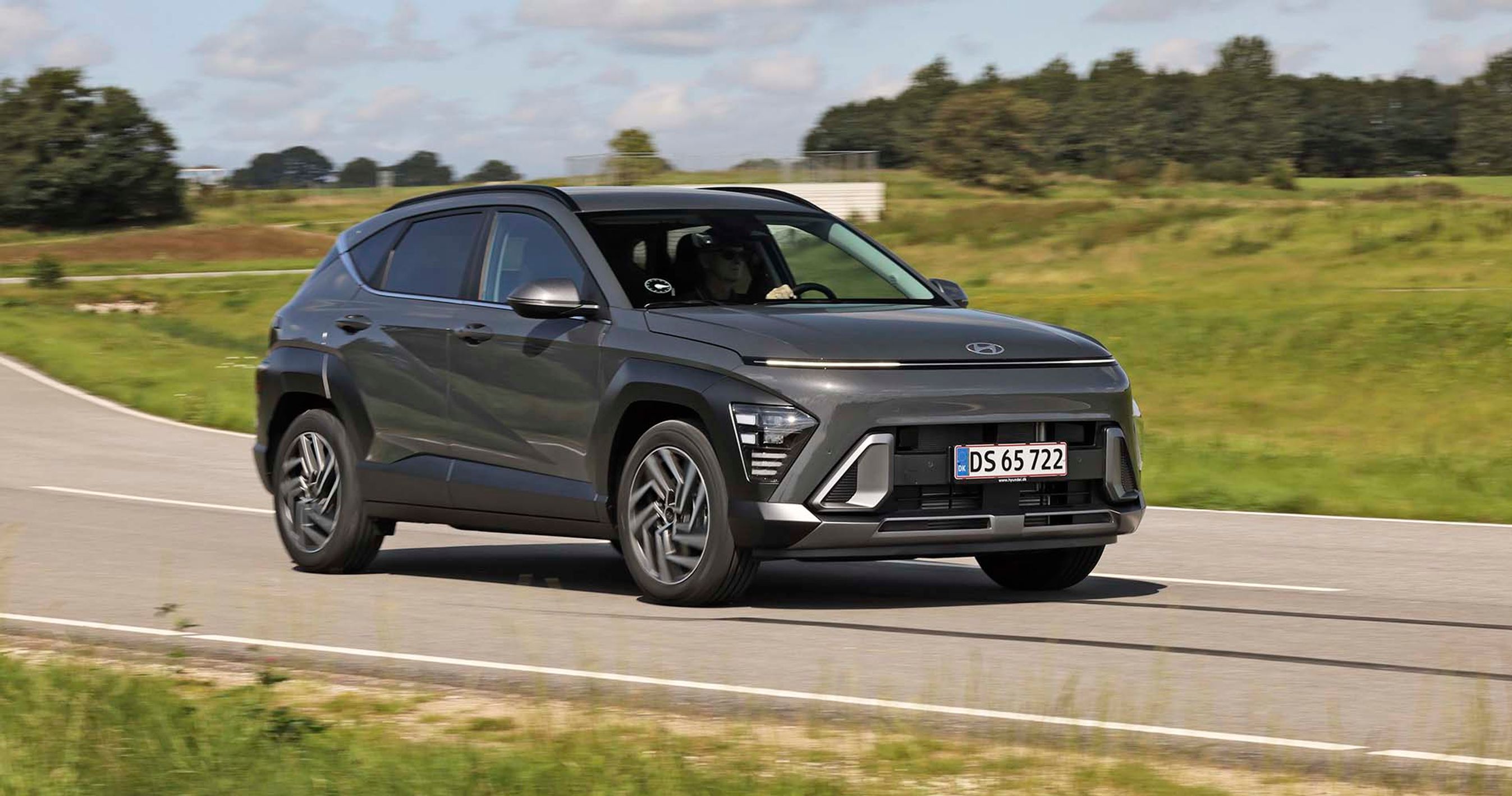 Hyundai Kona kører på landevej med græs i baggrunden.