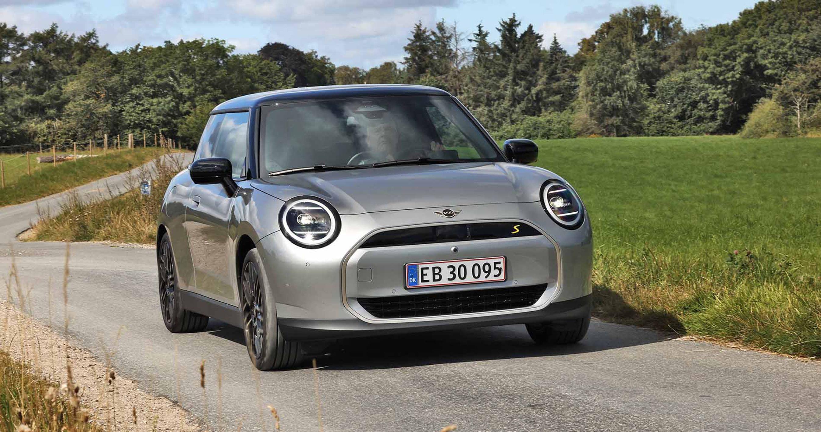 En sølvgrå Mini Cooper set forfra på en snoet, landlig vej.