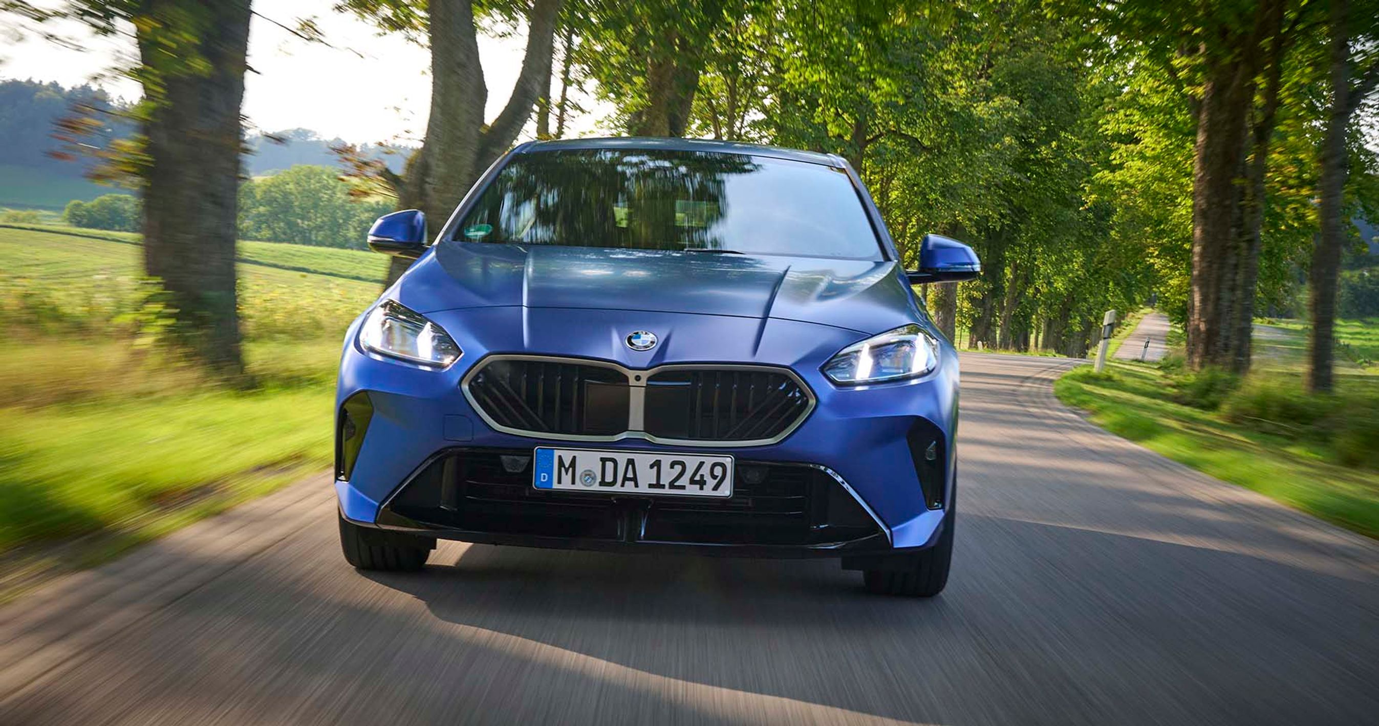 Blå BMW 1-serie set forfra, mens den kører på en allé