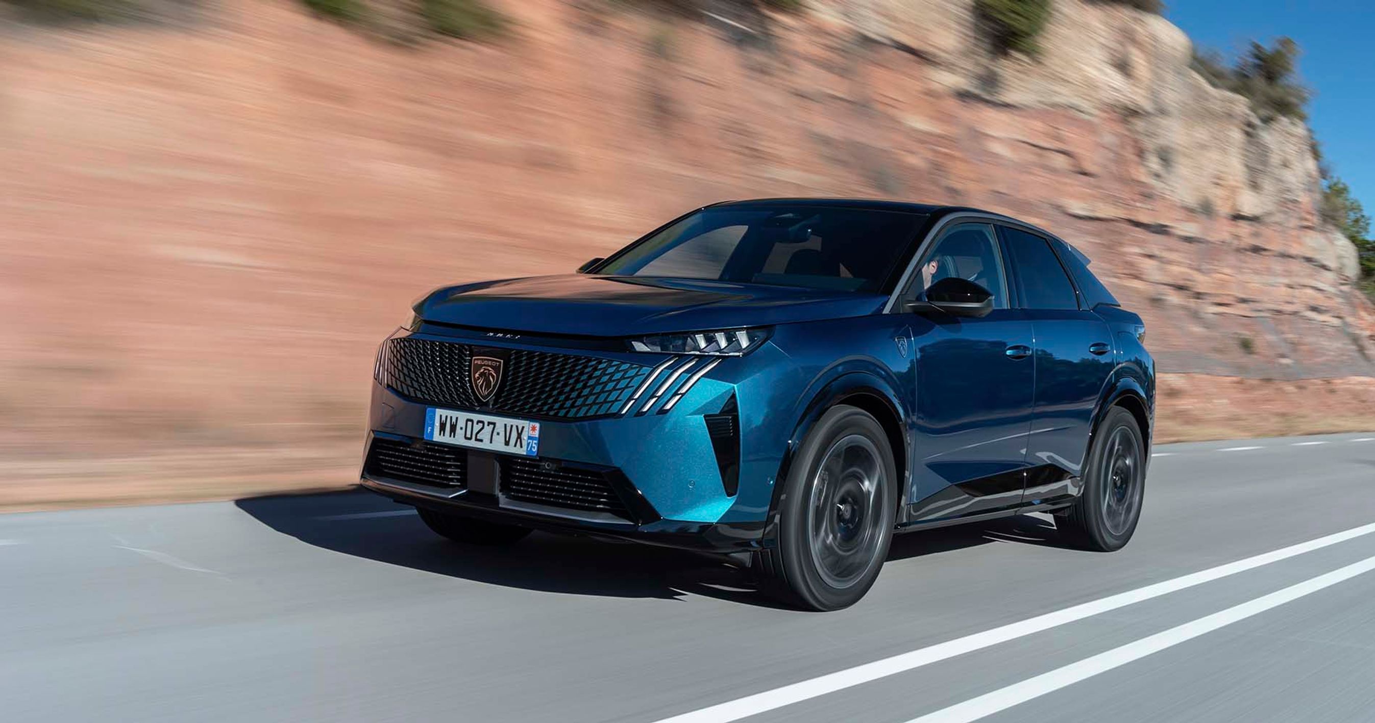 En Peugeot E-3008 elbil set forfra, mens den kører på en bjergvej med klipper i baggrunden