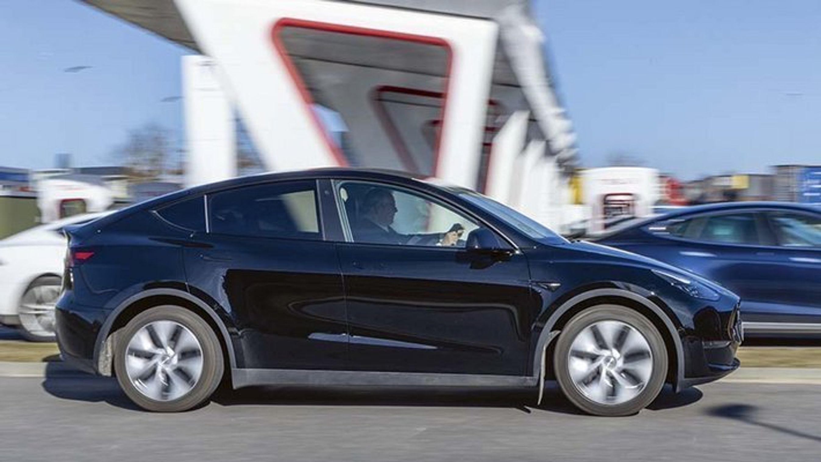 Tesla Model Y kører forbi en Tesla ladestation