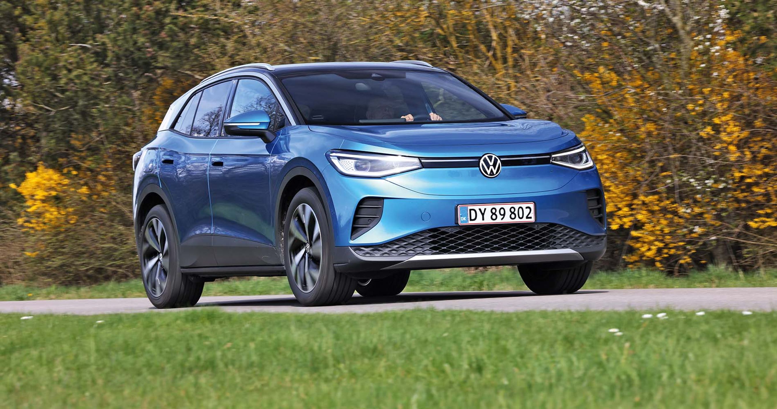Blå VW ID.4 kører på en landevej med træer i baggrunden