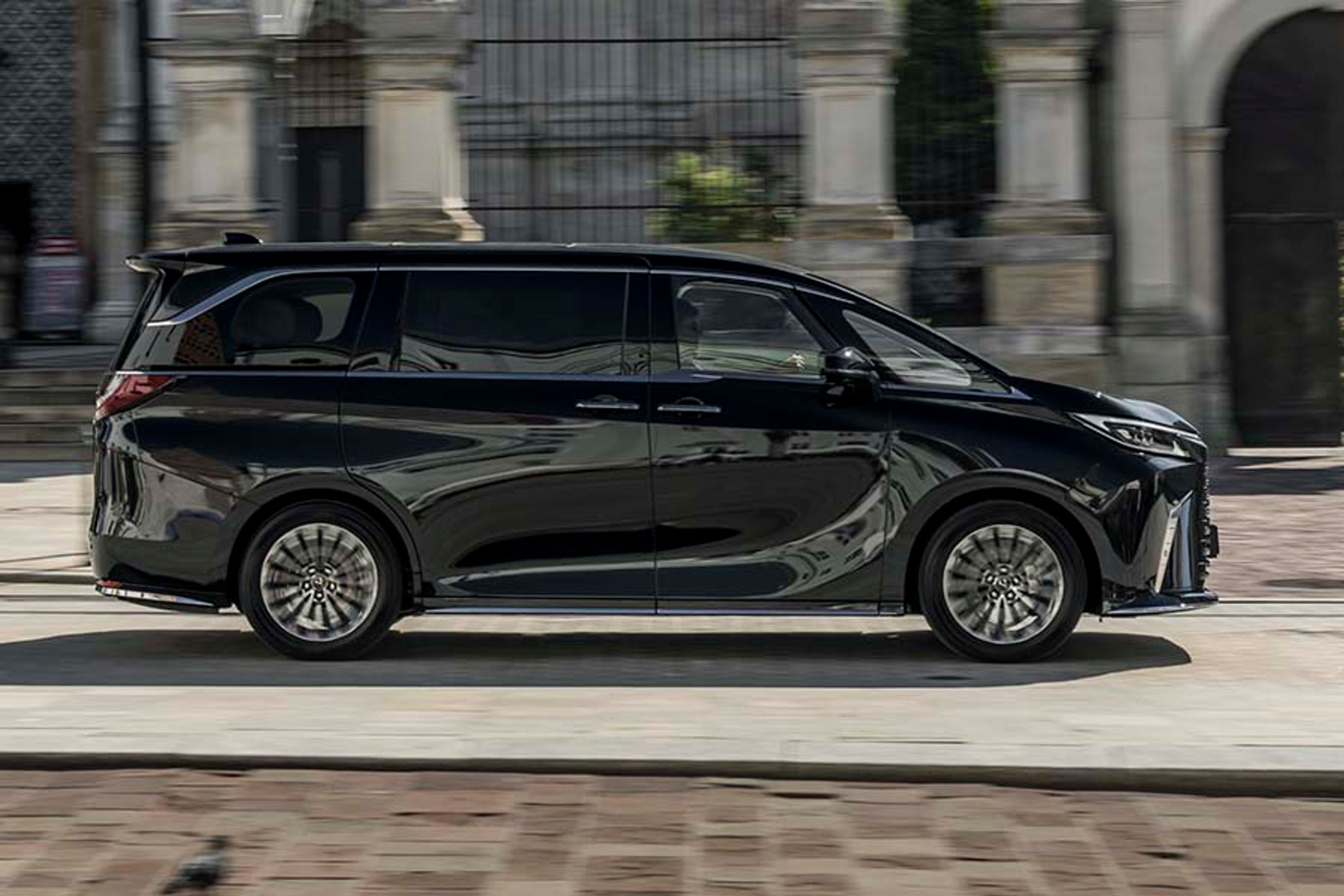 Lexus LM set fra siden, mens den kører på en vej med en bygning i baggrunden.