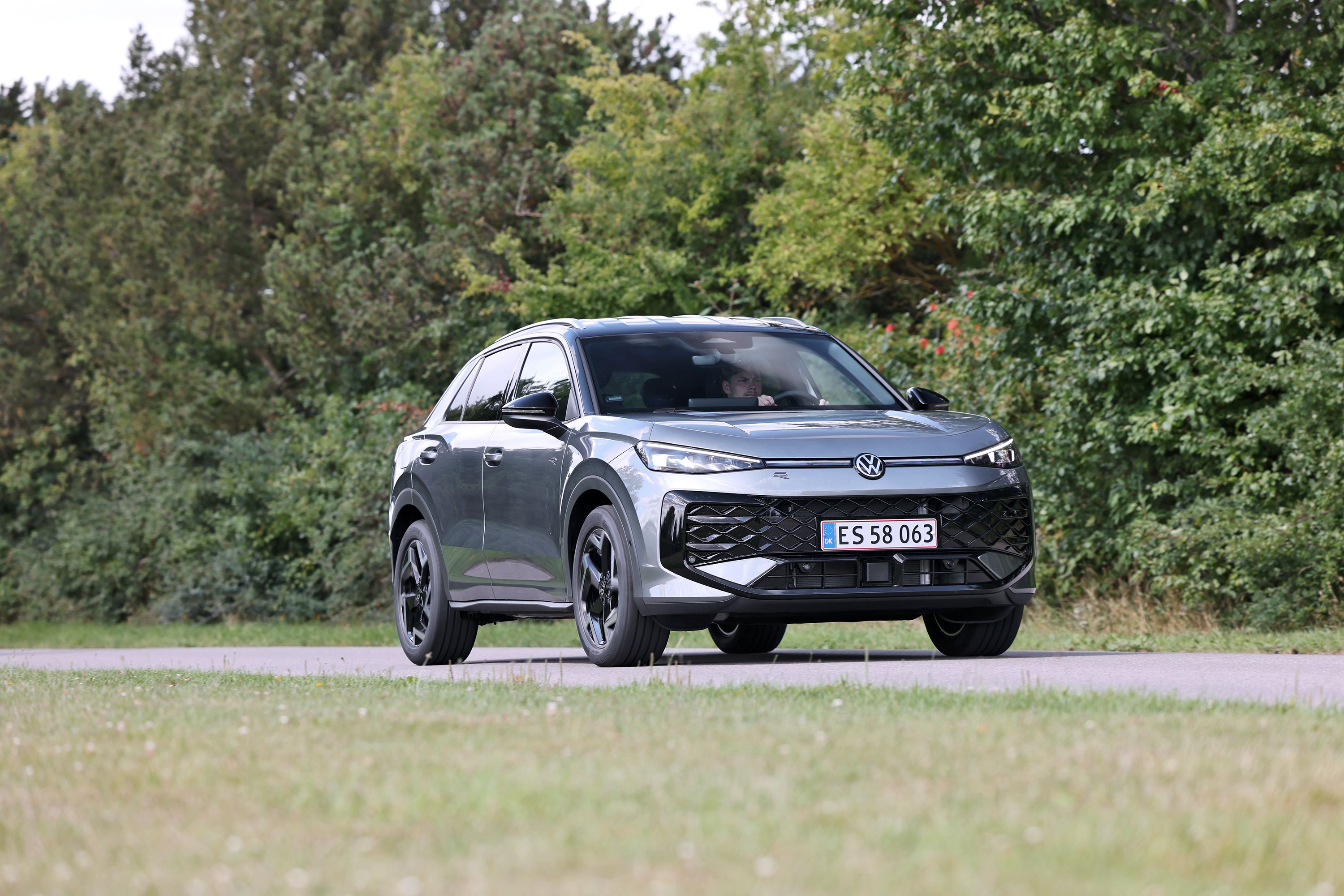 VW T-Roc fra 2026 kører på en landevej med grønne træer i baggrunden. 