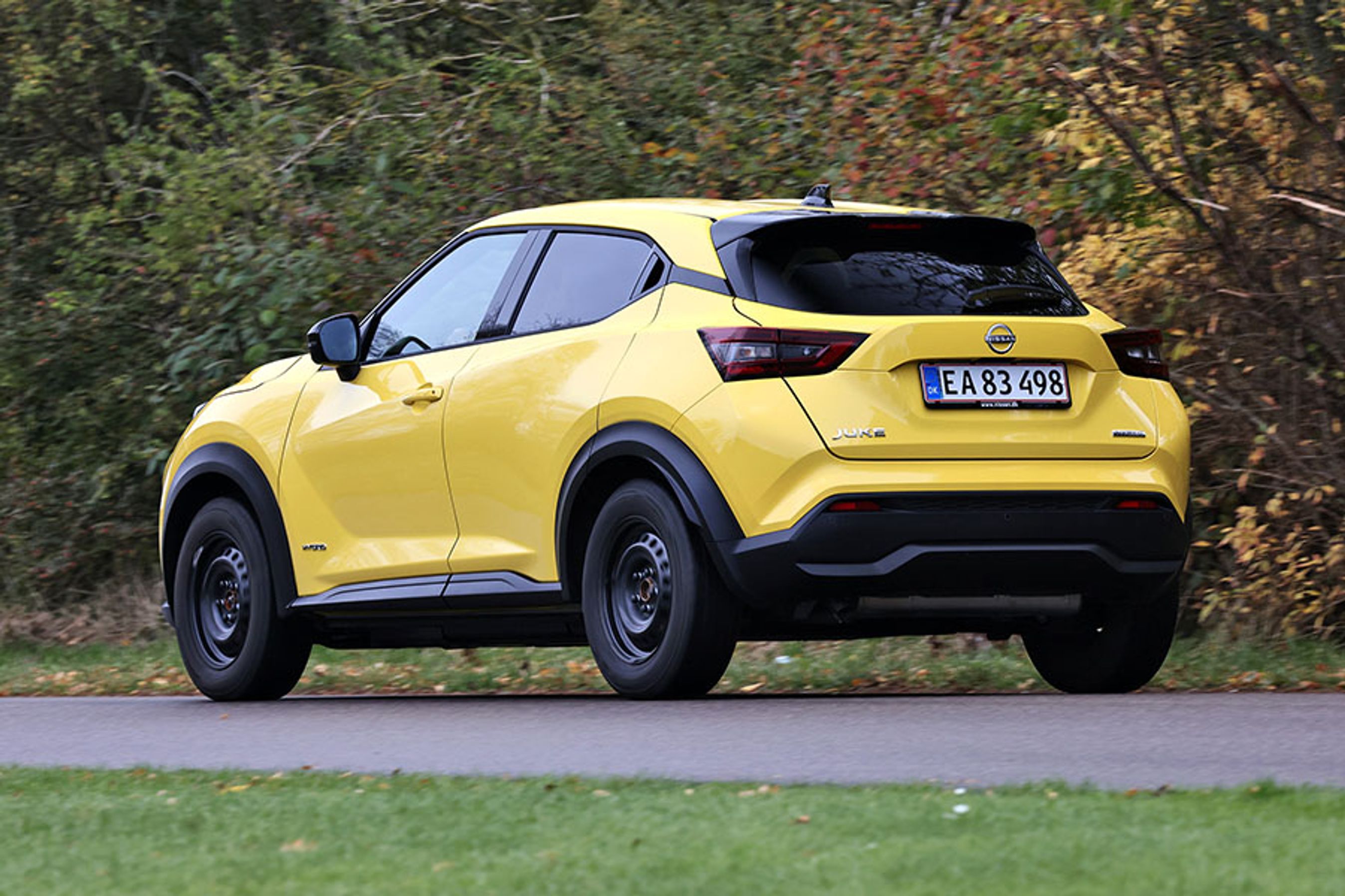Gul Nissan Juke set bagfra, mens den kører på landevej med træer i baggrunden