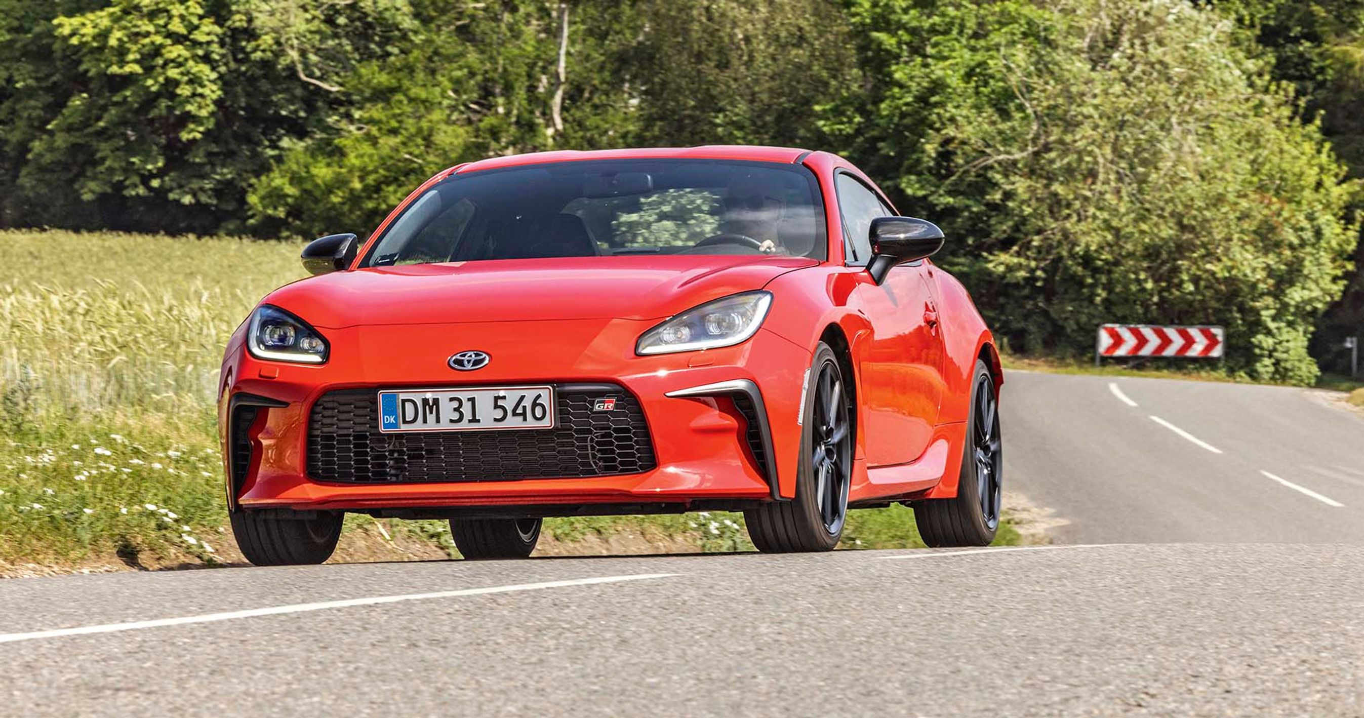 Rød Toyota GR86 kører på landevej med træer i baggrunden. 