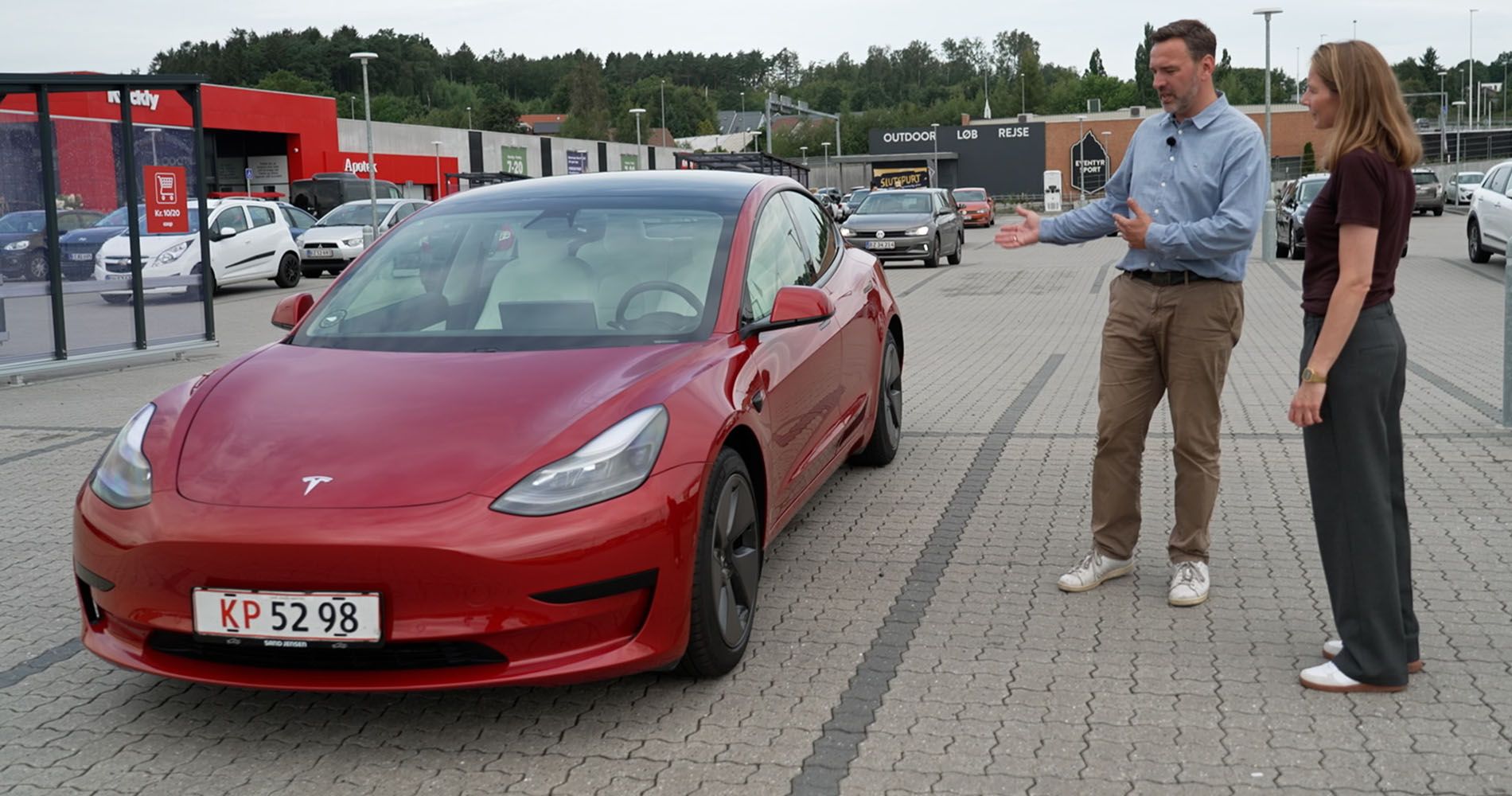 En mand og en dame kigger på en Rød Tesla Model 3
