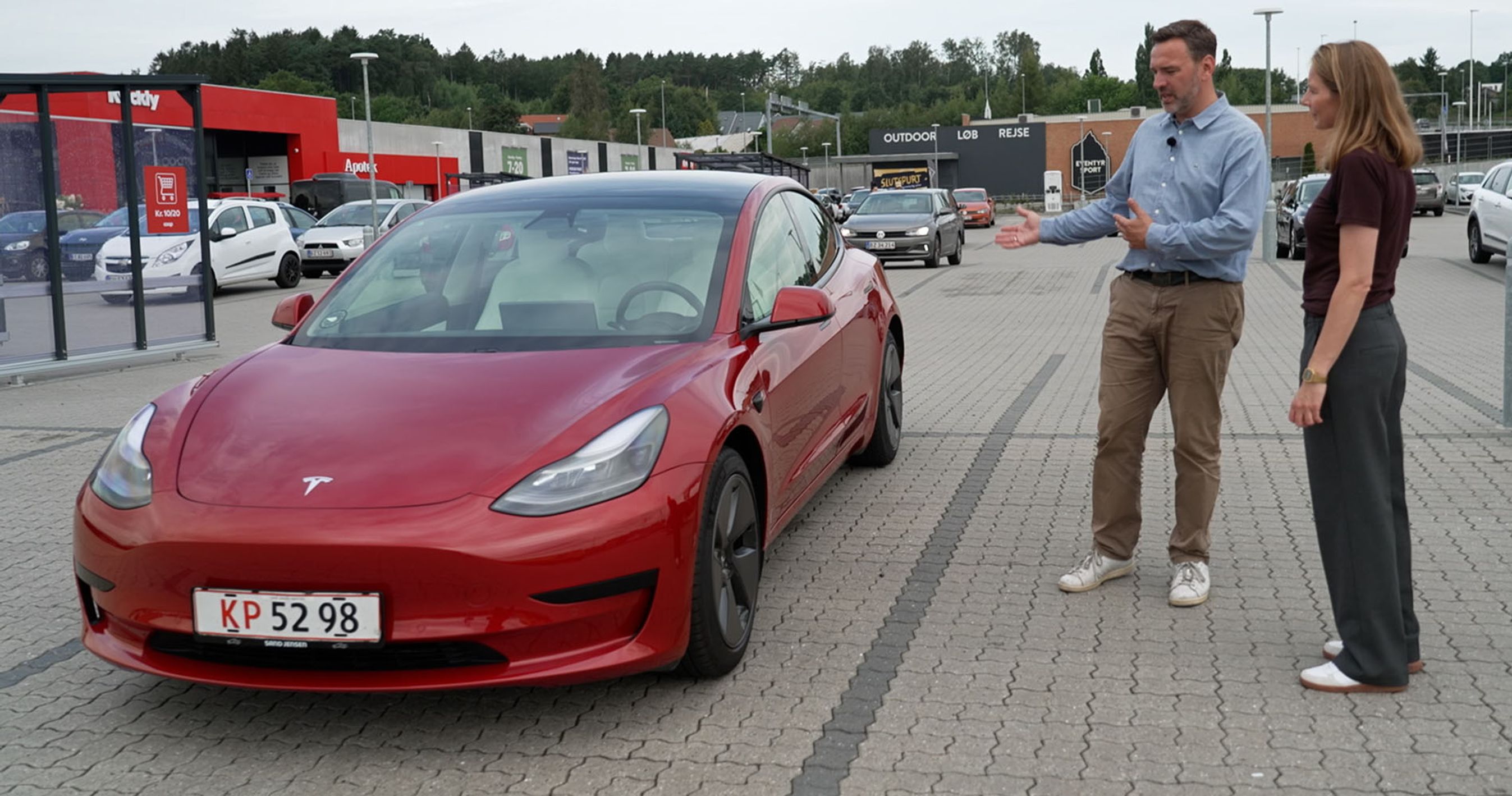 En mand og en dame kigger på en Rød Tesla Model 3