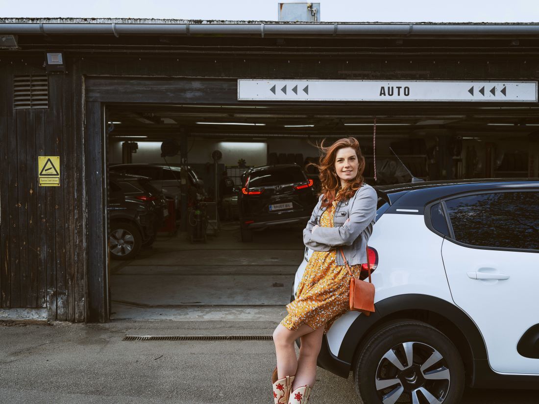 en kvinde står op af en bil, foran et værksted og overvejer hendes reparationsforsikring gennem FDM forsikringer