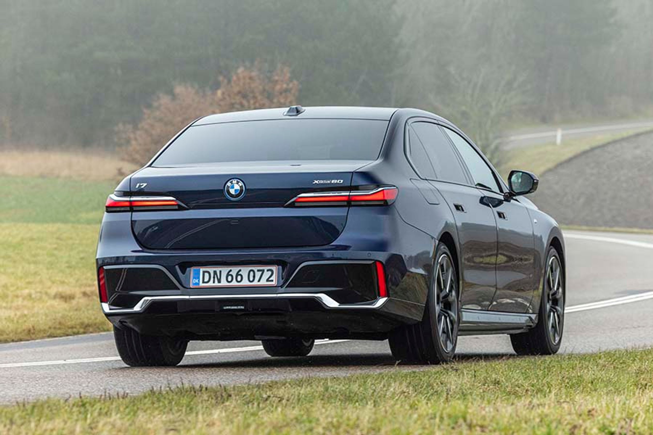 BMW i7 set bagfra, mens den køre på en snoet vej i tåge