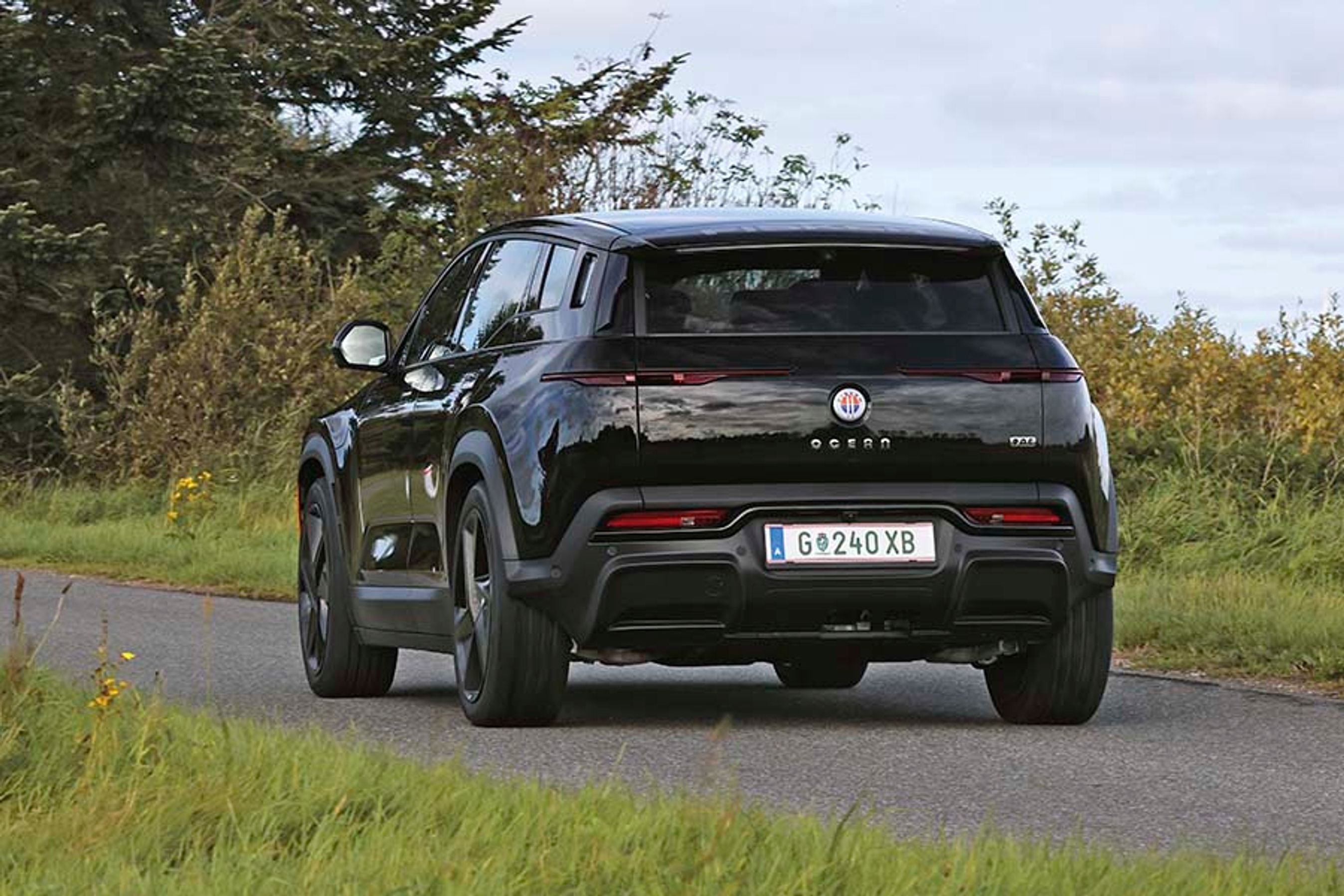 Elbilen Fisker Ocean set bagfra, mens den kører på en landevej med buske i baggrunden.