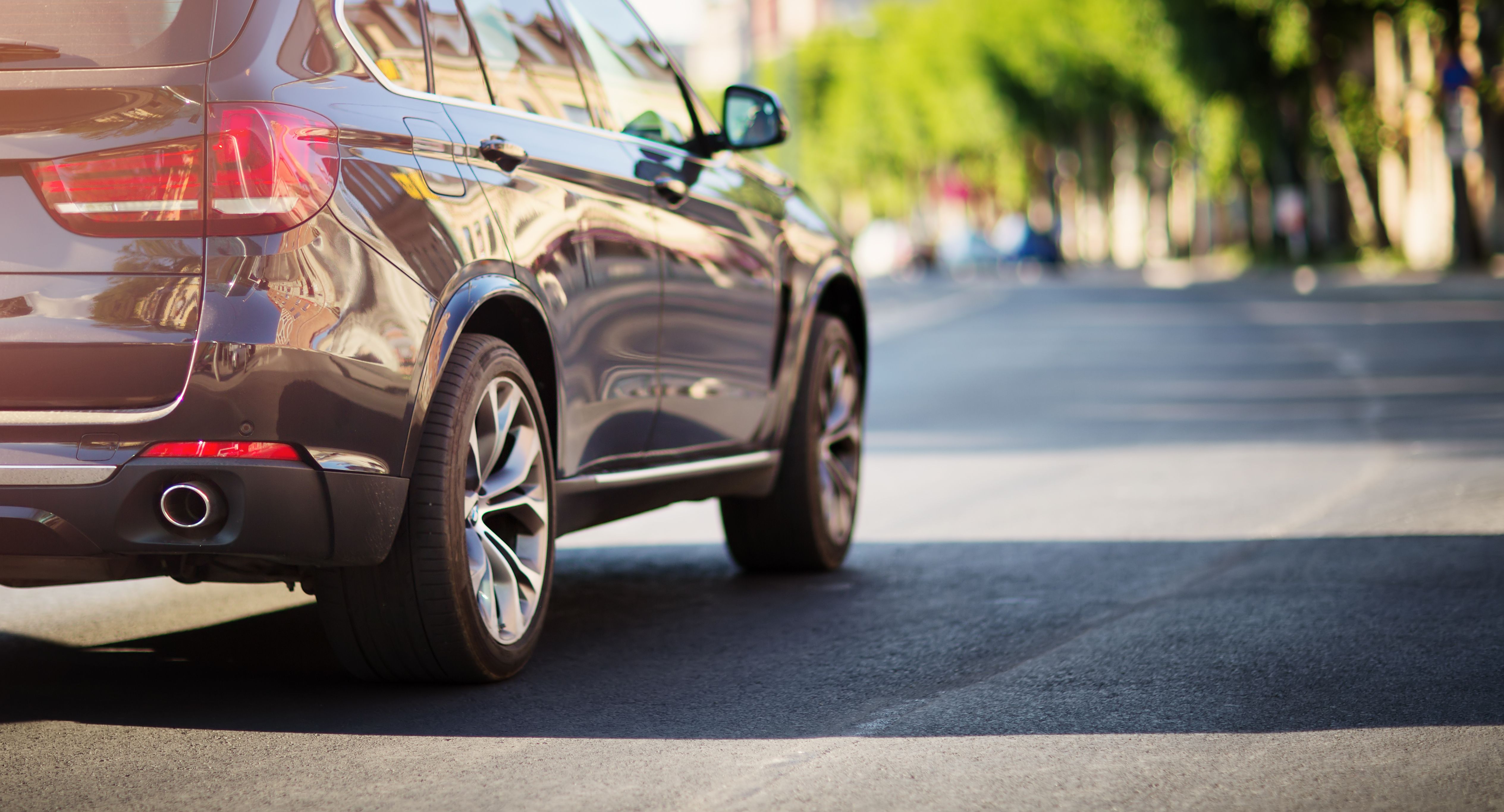 Sort bil kører på en vej der er omgivet af grønne træer