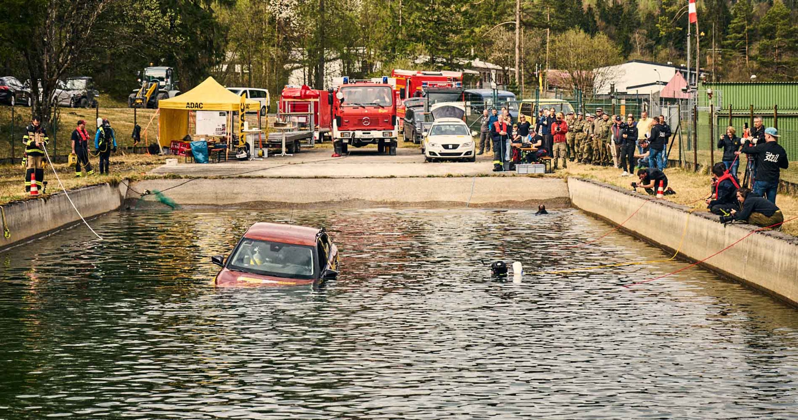 Bil kører i vandet under test, hvor redningsfartøjer holder klar