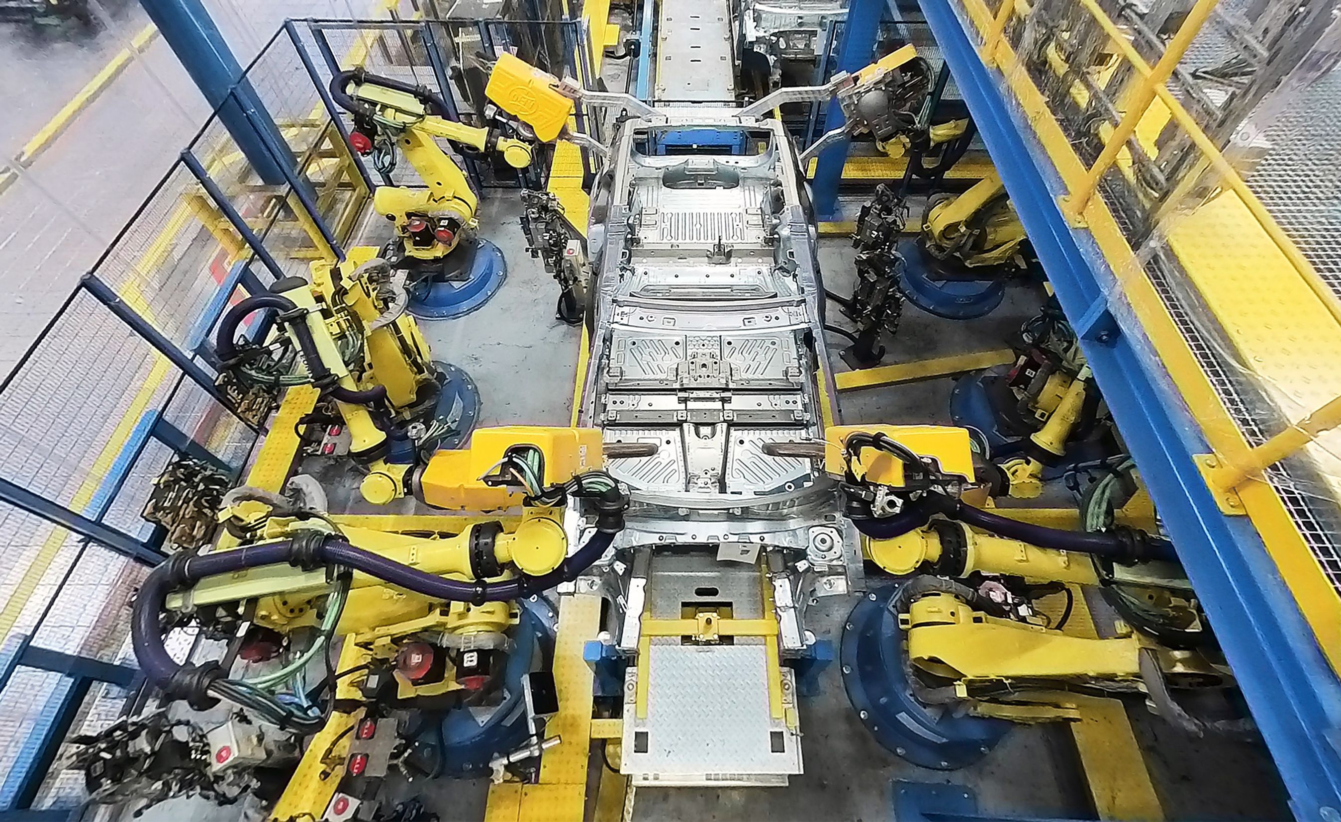 Elbil på samlebånd med gule robotter.