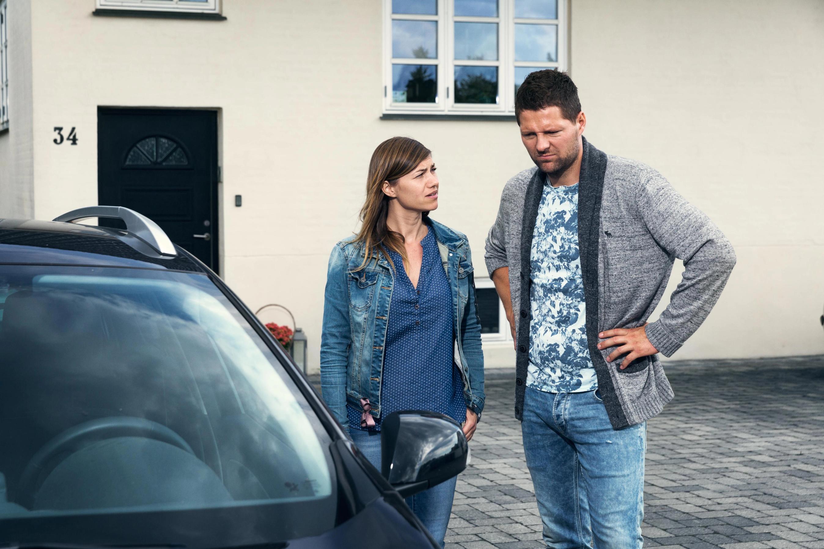 Par står udenfor og kigger skeptisk på deres bil.