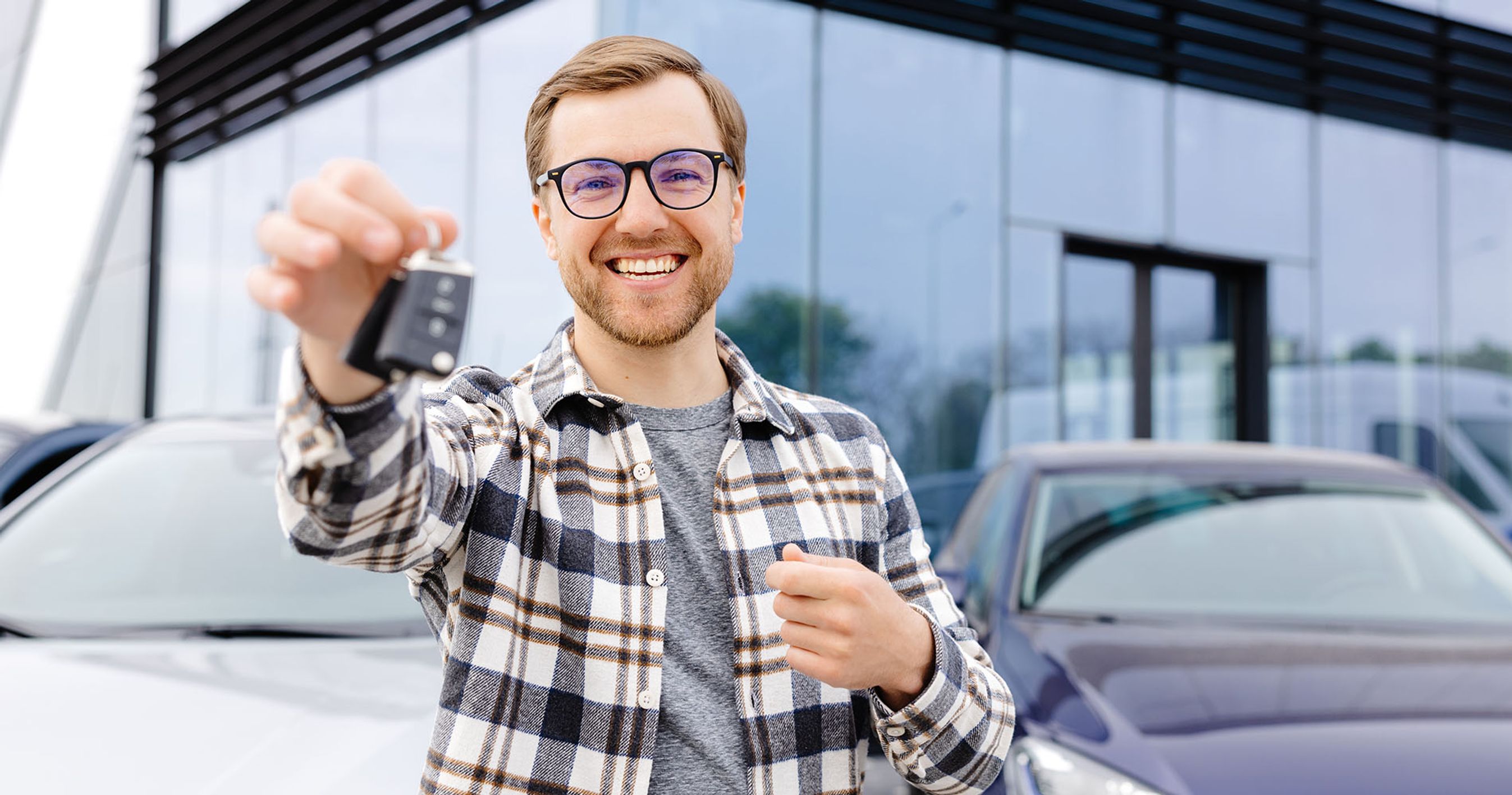 Mand med briller står med bilnøgle i hånden foran en bilforhandler.