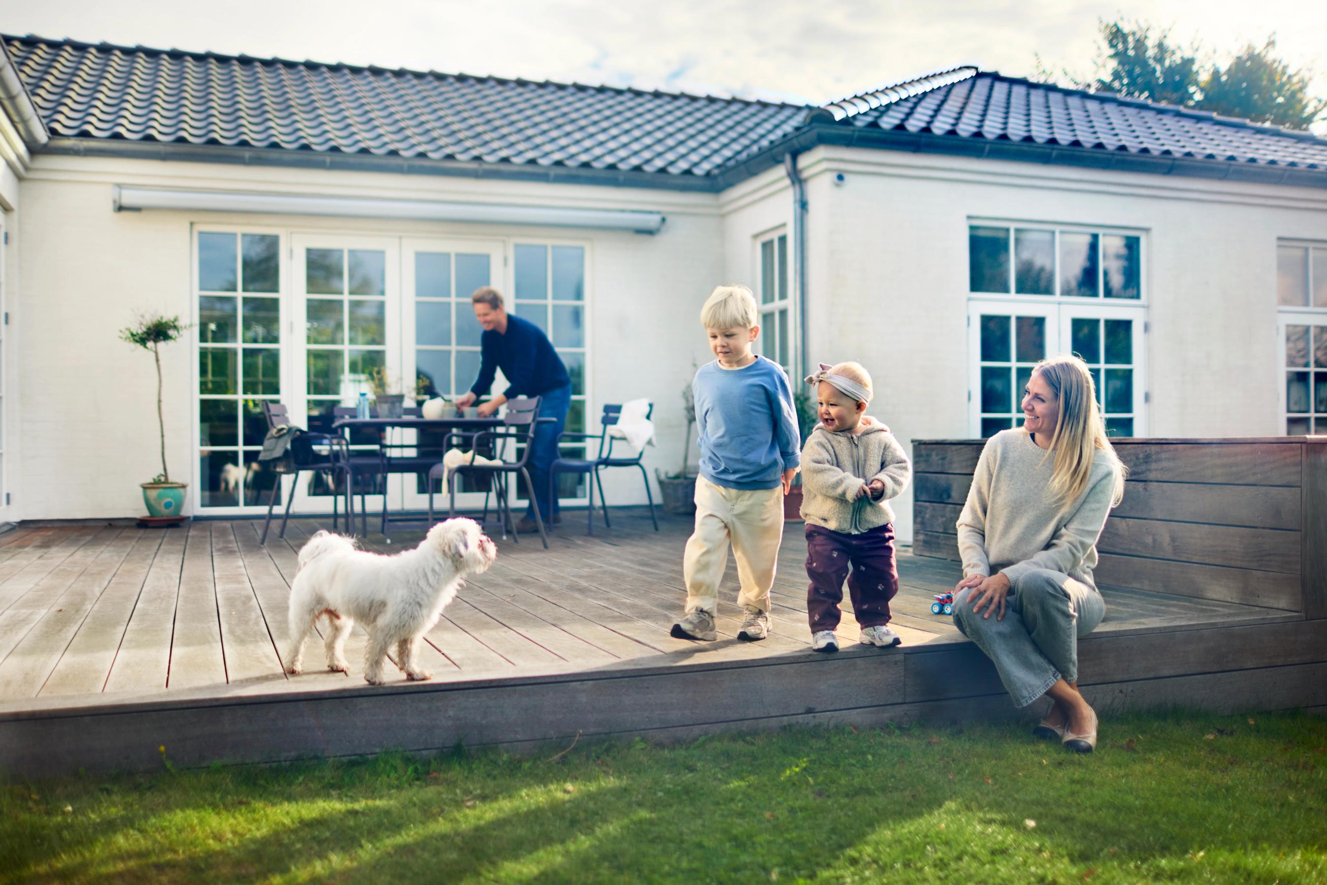 Familie sidder på terassen ved deres hus, sammen med deres hund - forsikring fra FDM