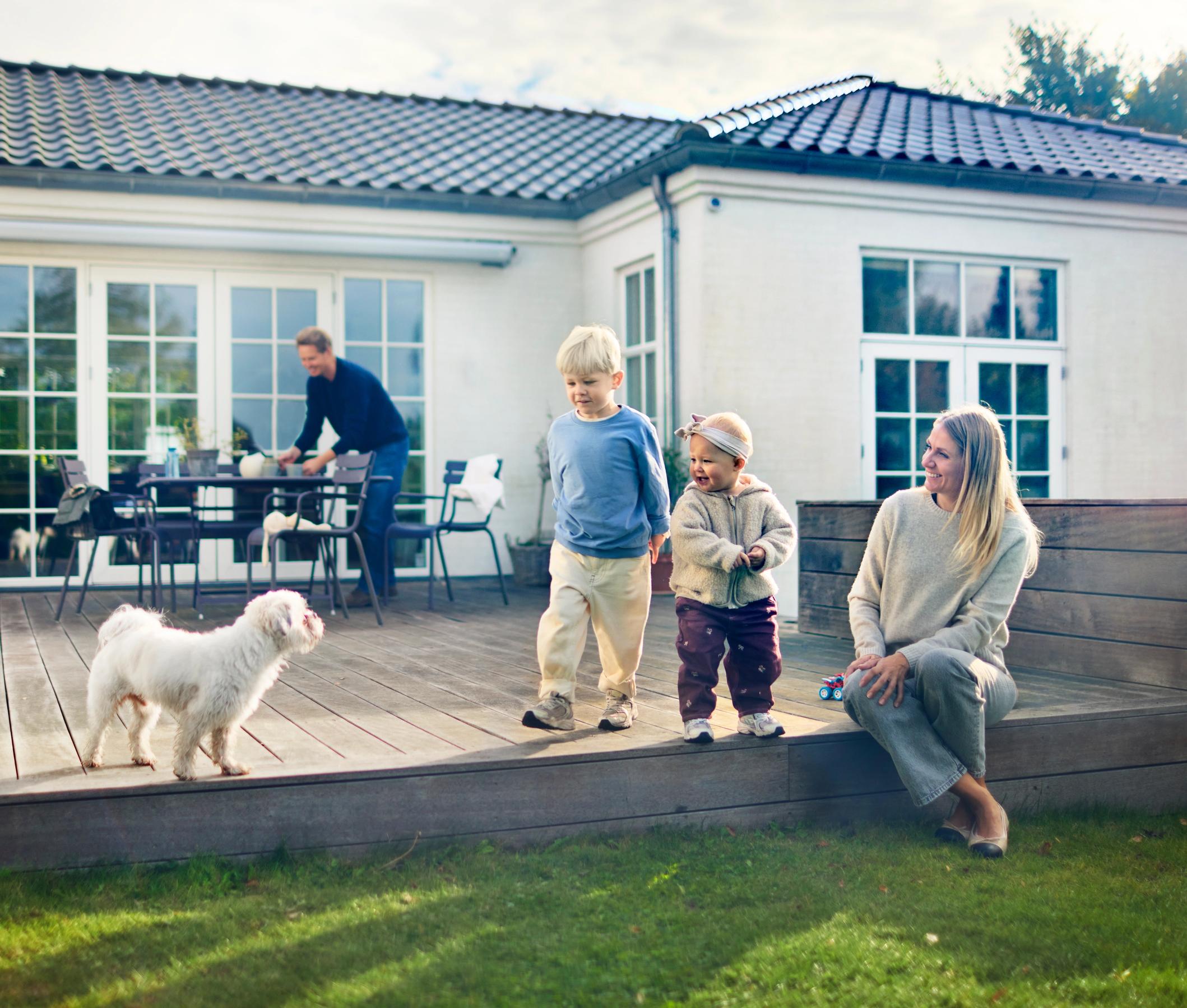 Familie sidder på terassen ved deres hus, sammen med deres hund - forsikring fra FDM