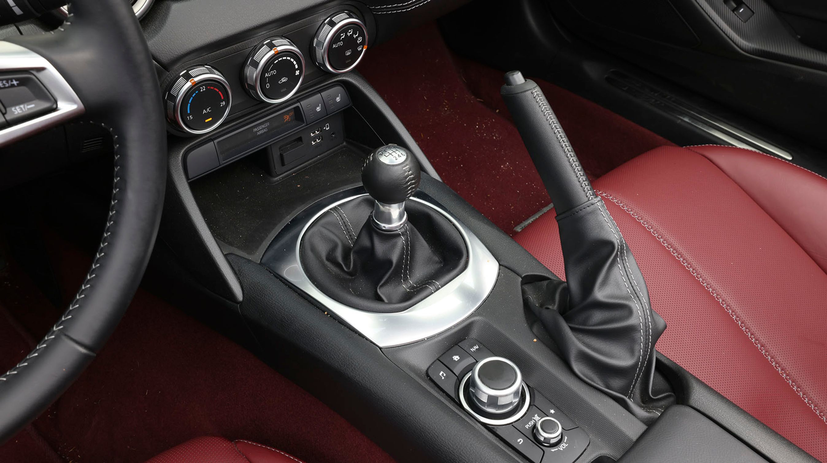 En af det helt store glæder i MX-5 er gearskiftet. Det er en sand fornøjelse, fordi det går let samtidig med, at der er en mekanisk fornemmelse i selve skiftet. Den runde, sølvfarvede knap benyttes til at styre info-skærmen.