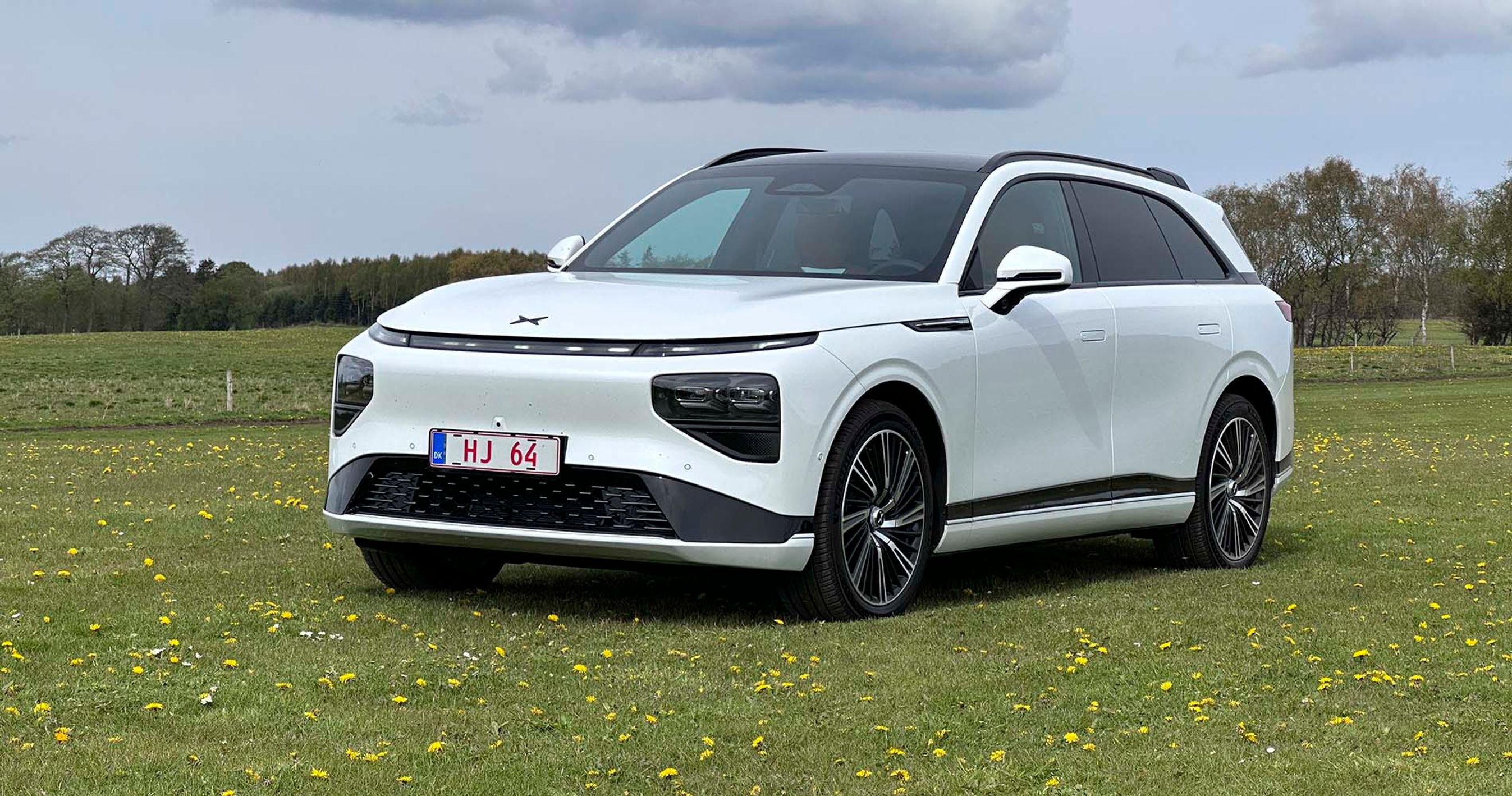 En hvid Xpeng G9 holder parkeret på en græsplæne med træer i baggrunden