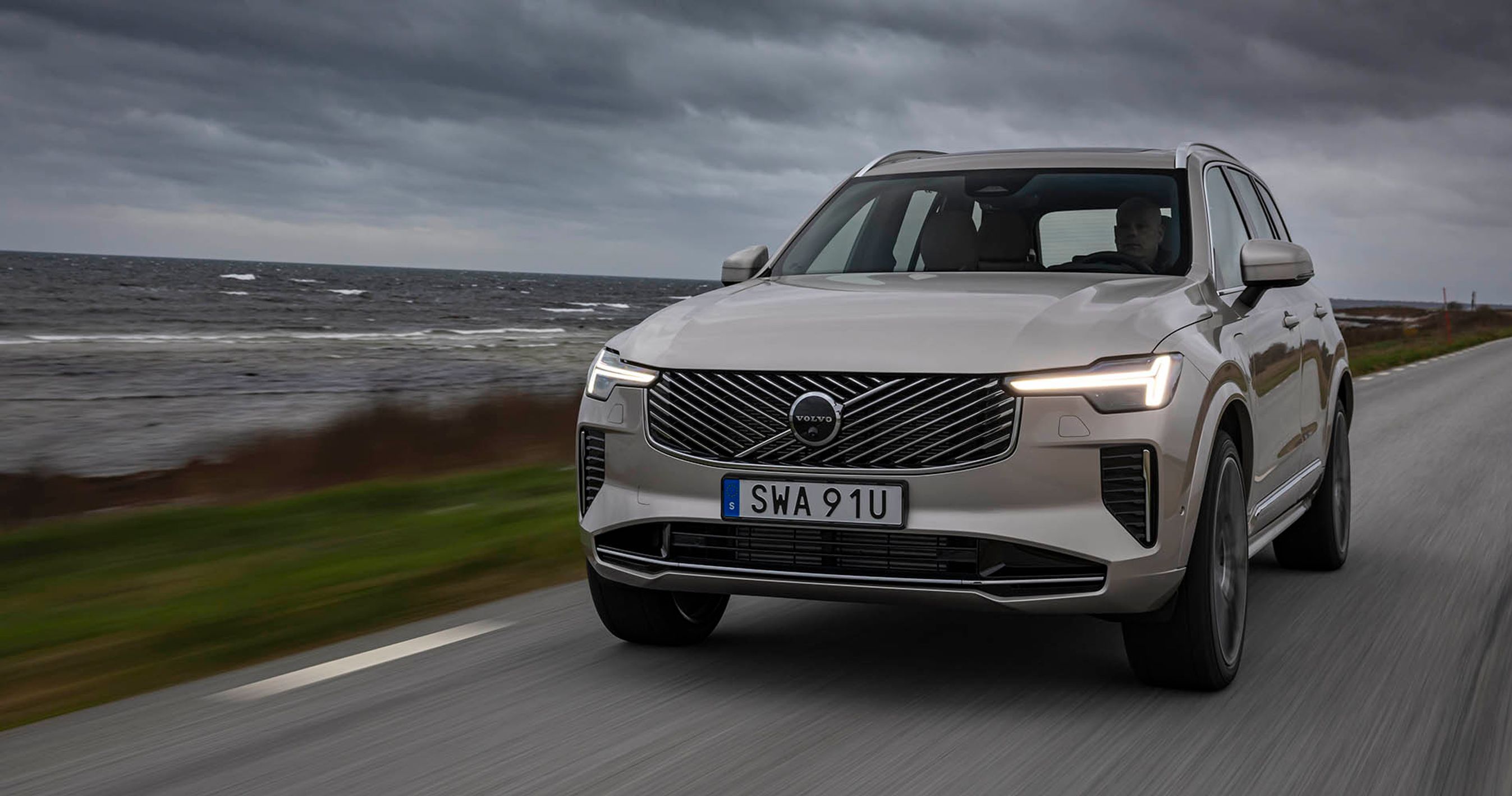 Volvo XC90 set forfra, mens den kører på kystvej med dramatiske skyer i baggrunden.