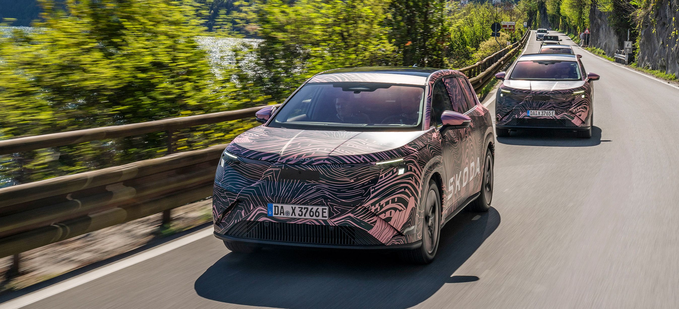 To kamuflerede SUV-biler kørende med sø og bjerge i baggrunden.