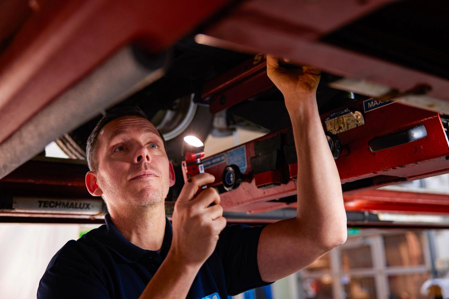 Testassistent lyser på bilens motor og gennemgår bilen ved bilsyn