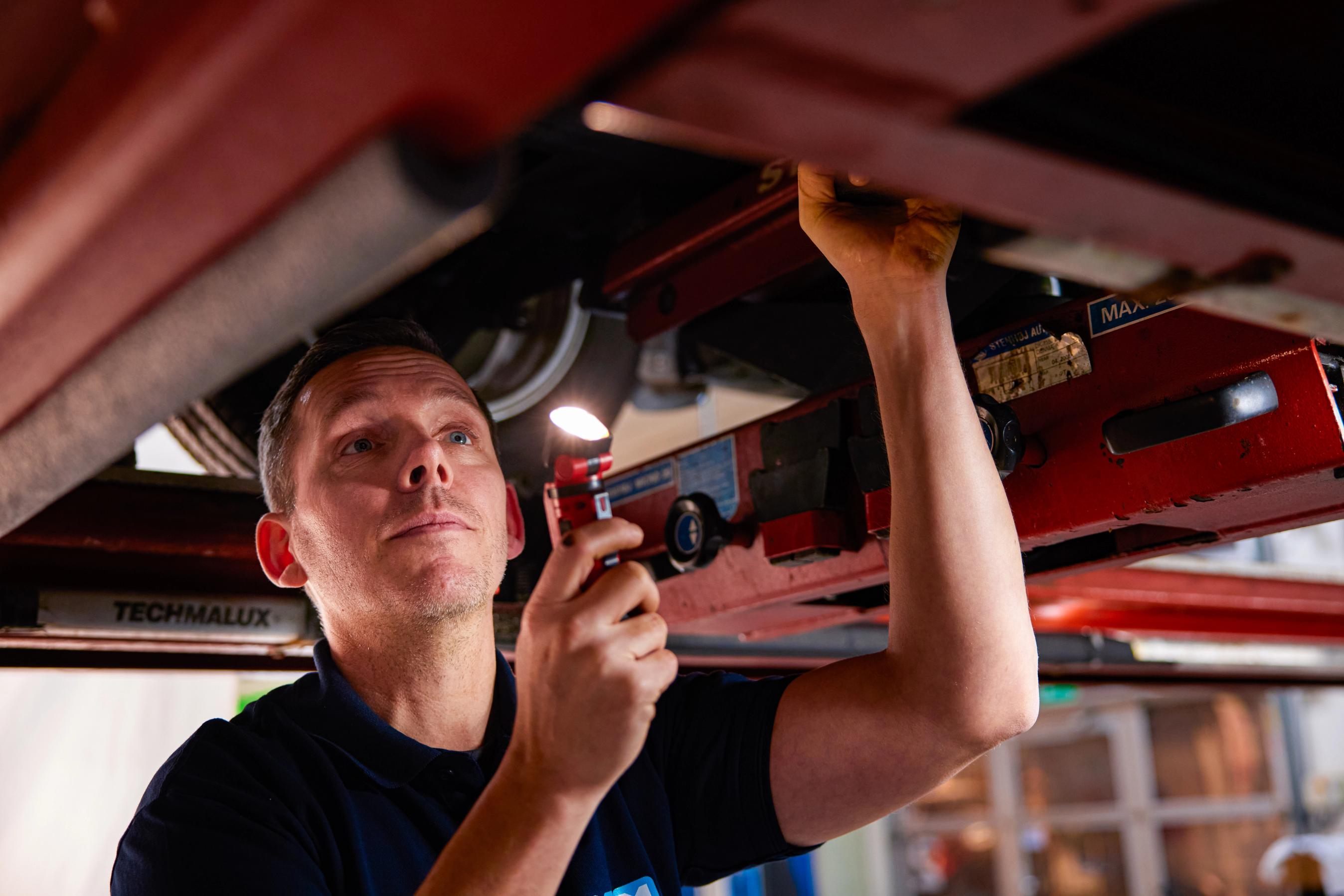 Testassistent lyser på bilens motor og gennemgår bilen ved bilsyn